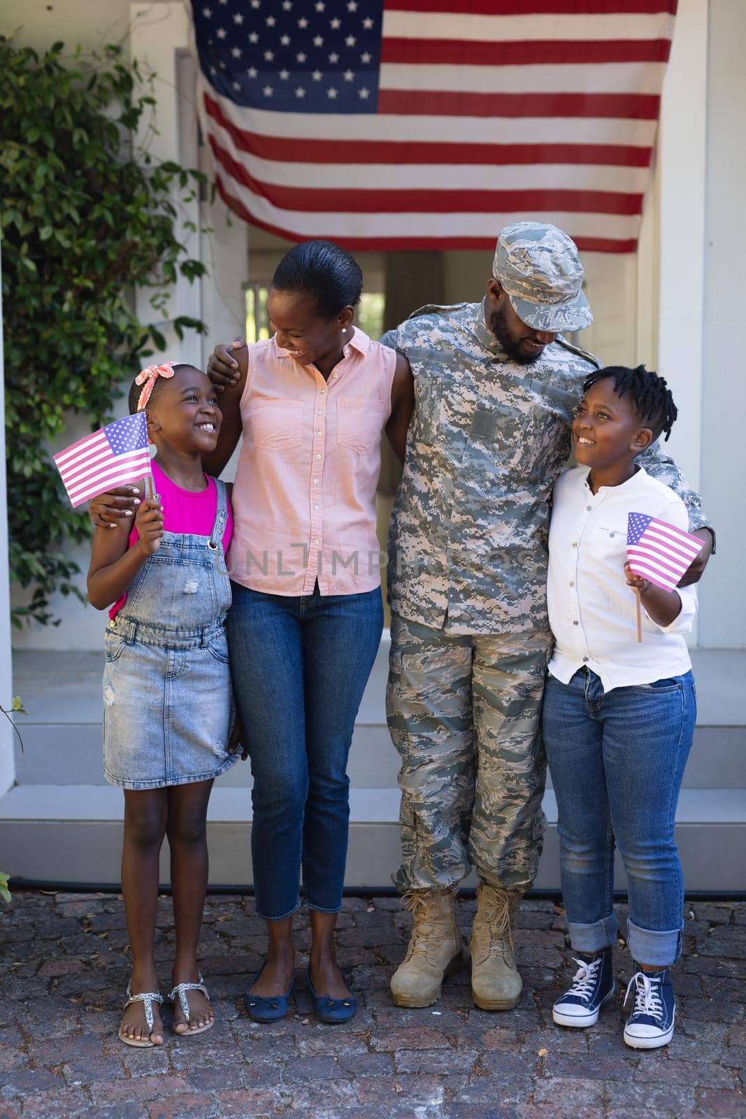 Smiling african american soldier father hugging wife and children in front of house. soldier returning home to family.