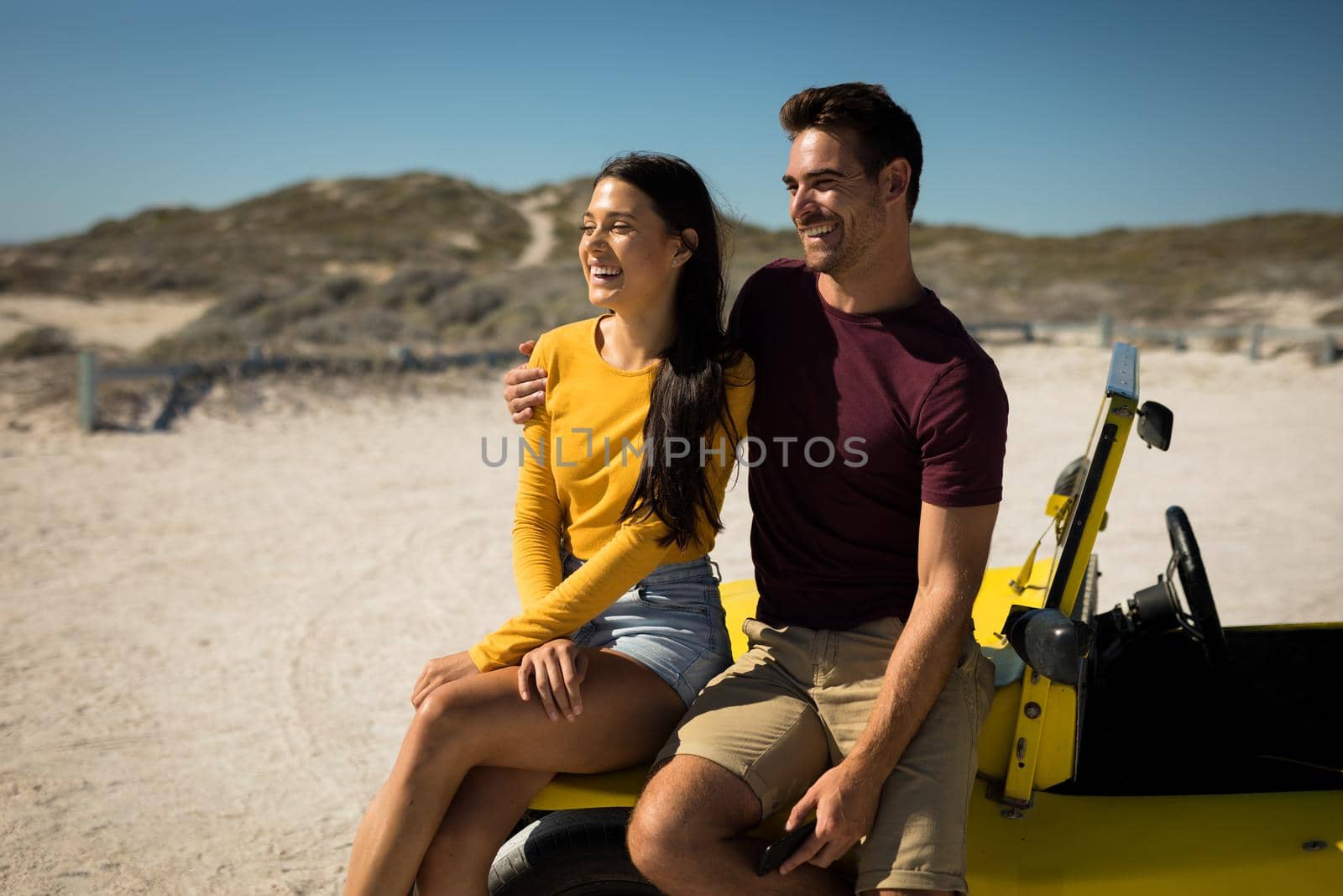Happy caucasian couple sitting on beach buggy by the sea smiling by Wavebreakmedia