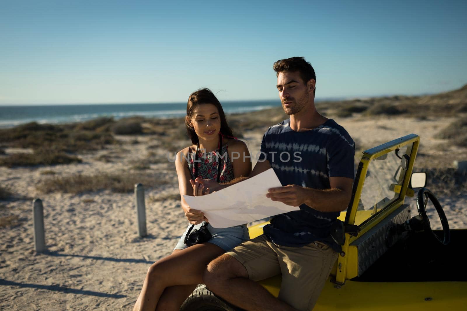 Happy caucasian couple sitting on beach buggy by the sea reading roadmap. beach break on summer holiday road trip.
