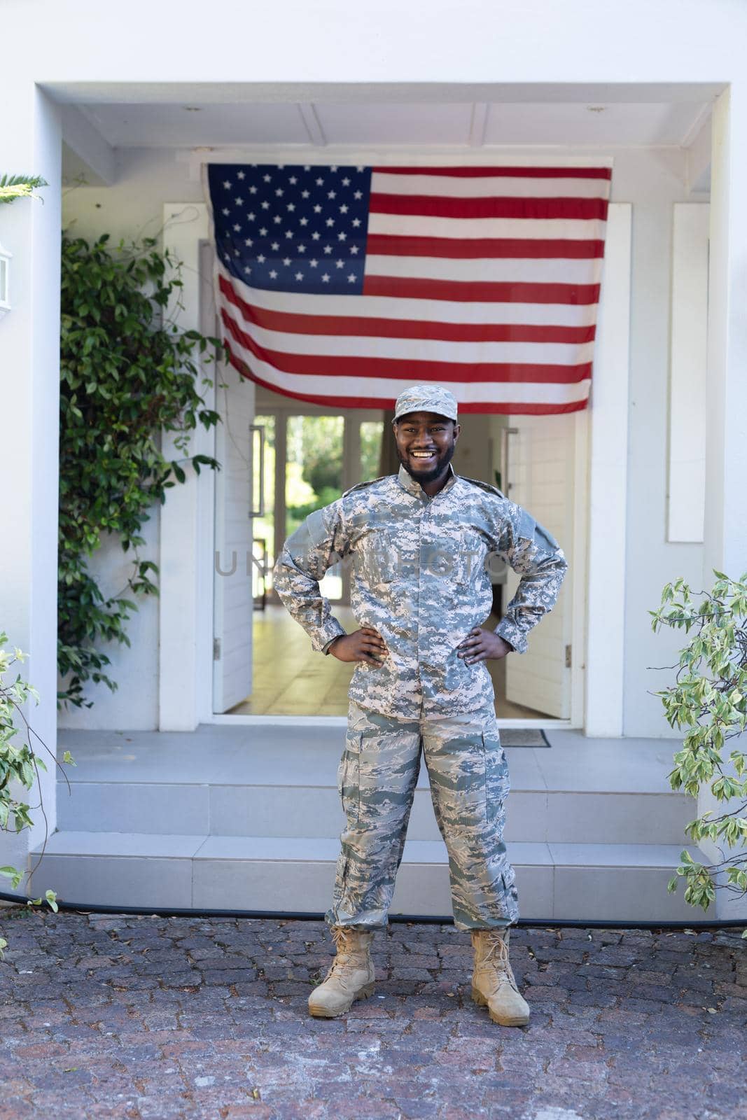 Smiling african american male soldier standing in front of american flag outside home. soldier returning home to family.