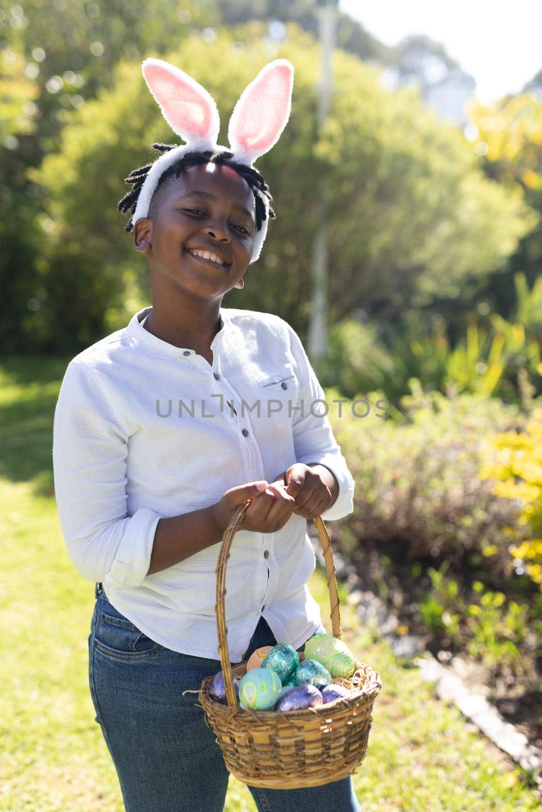 Portrait of smiling african american boy holding basket while easter egg hunting. celebrating easter at home in isolation during quarantine lockdown.