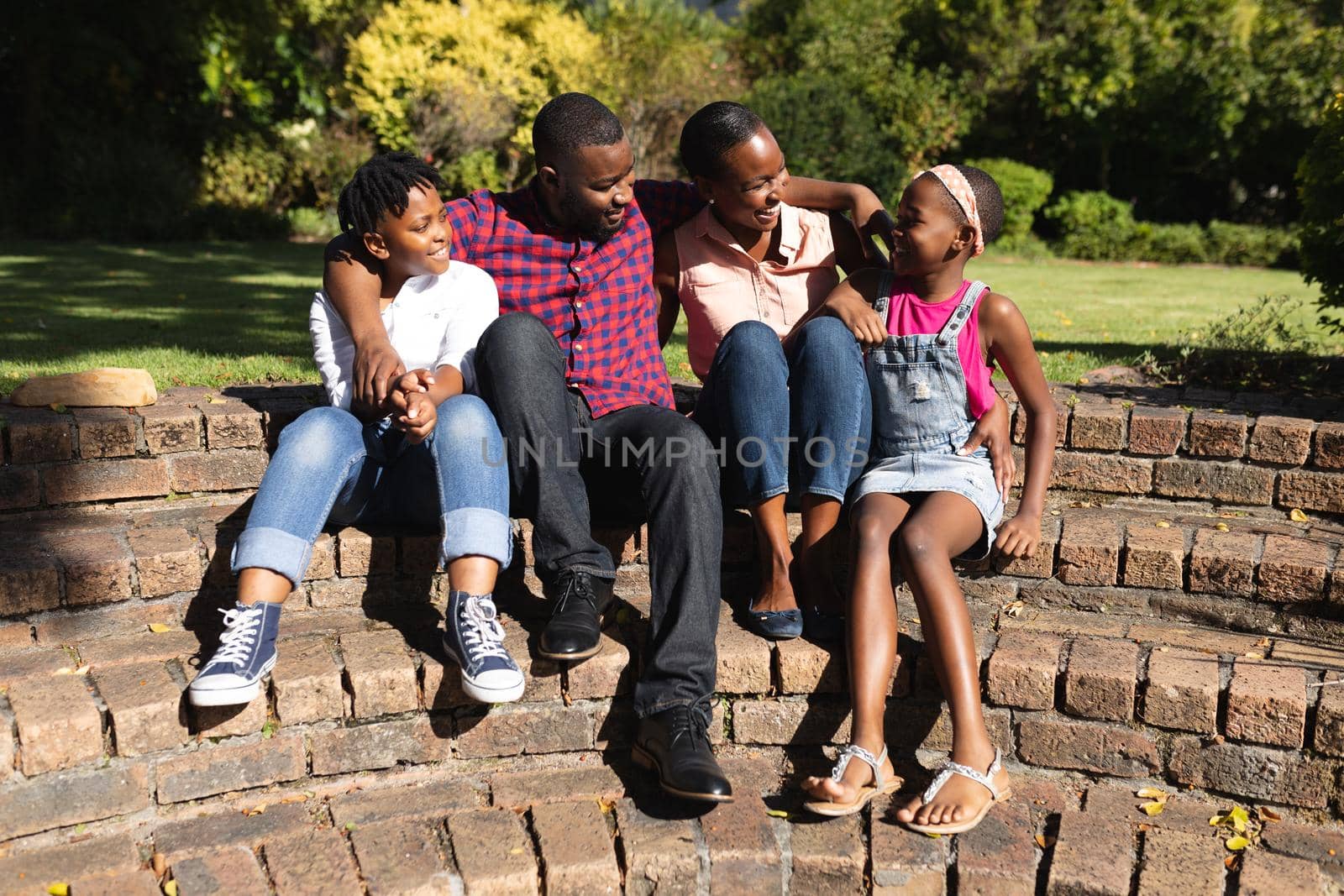 Smiling african american parents with daughter and son sitting embracing outdoors. staying at home in isolation during quarantine lockdown.