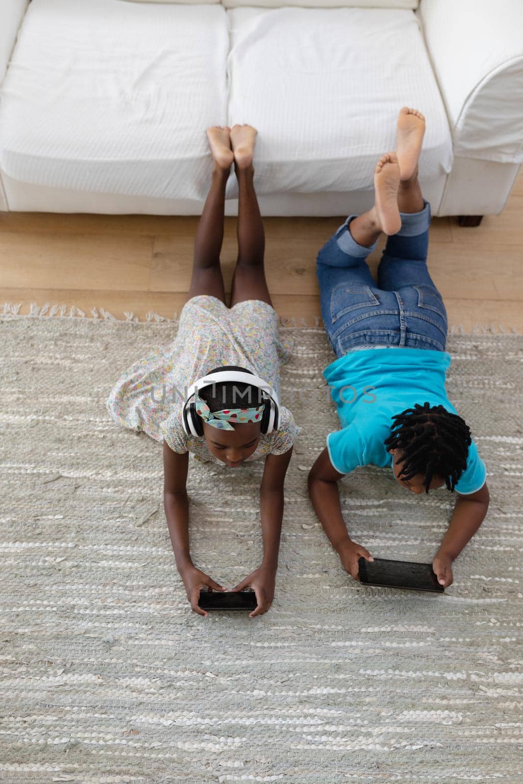 African american brother and sister wearing headphones lying on floor using smartphones by Wavebreakmedia