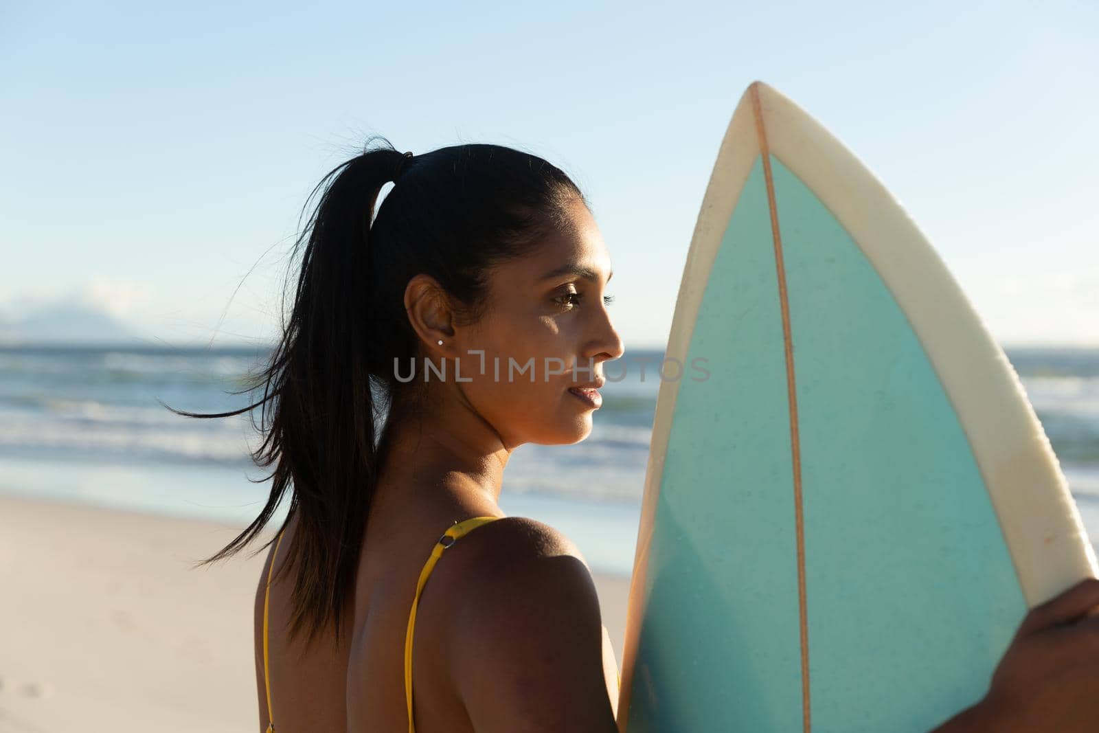 Mixed race woman carrying surfboard on the beach. healthy outdoor leisure time by the sea.