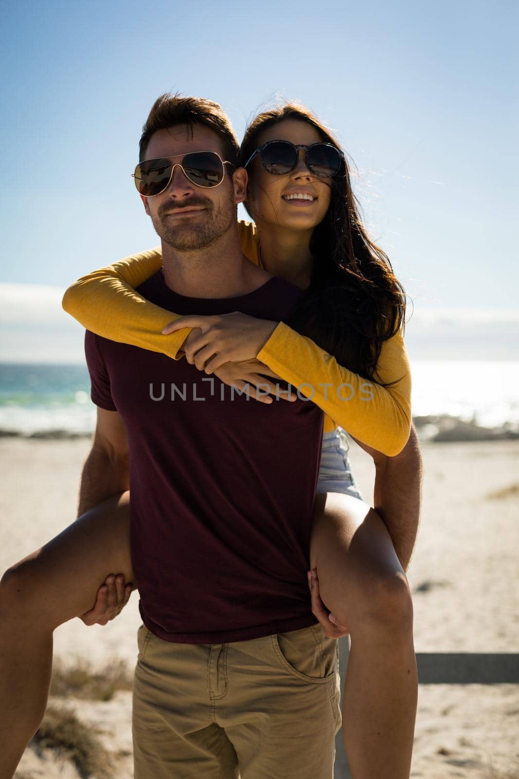 Happy caucasian couple on beach by the sea wearing sunglasses smiling by Wavebreakmedia