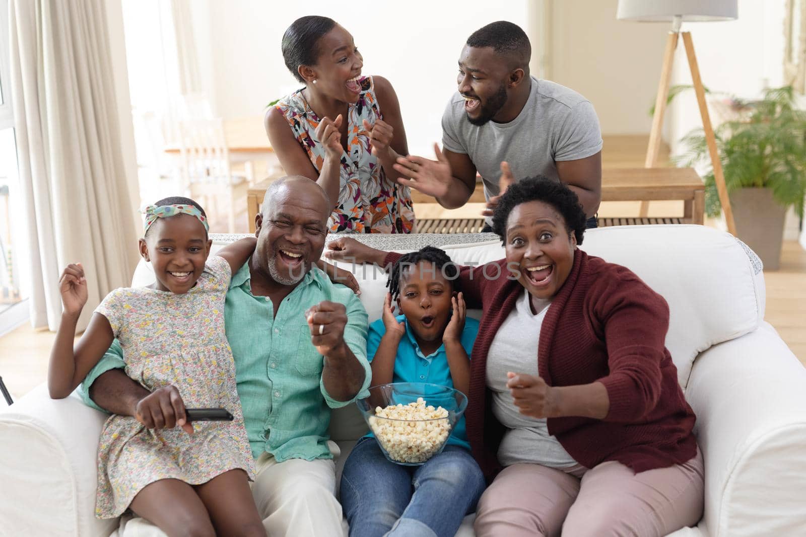 Excited african american parents, grandparents and grandchildren on couch watching tv and cheering by Wavebreakmedia
