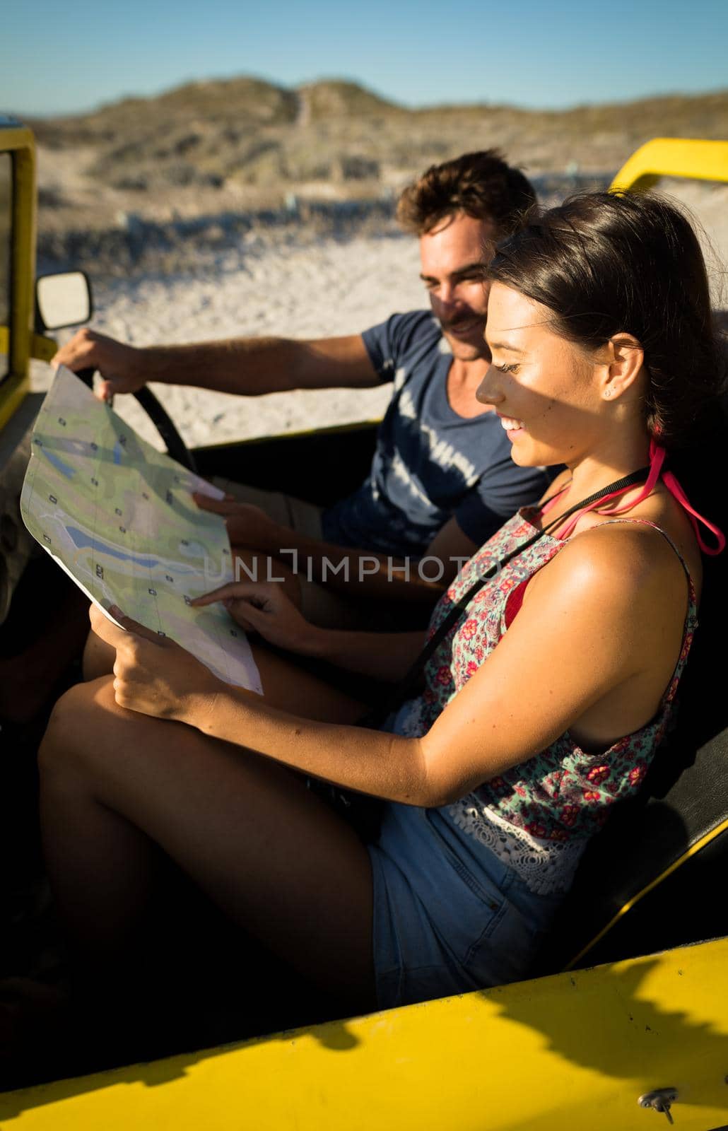Happy caucasian couple sitting in beach buggy by the sea reading roadmap. beach break on summer holiday road trip.