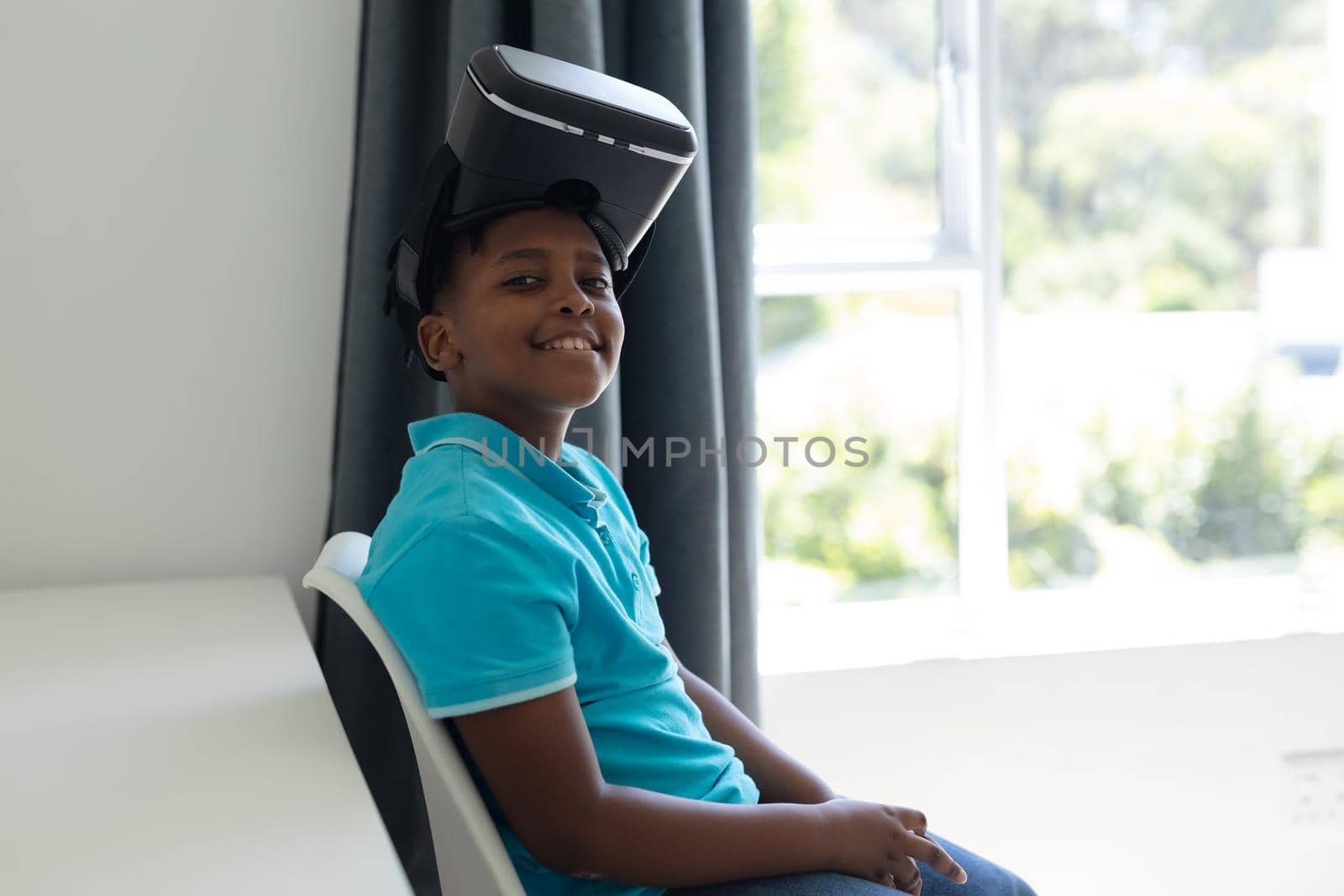 Portrait of smiling african american boy wearing vr headset raised on top of his head. staying at home in isolation during quarantine lockdown.