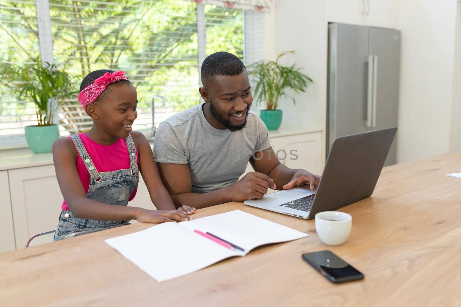 African american father and daughter sitting with laptop working from home. staying at home in isolation during quarantine lockdown.