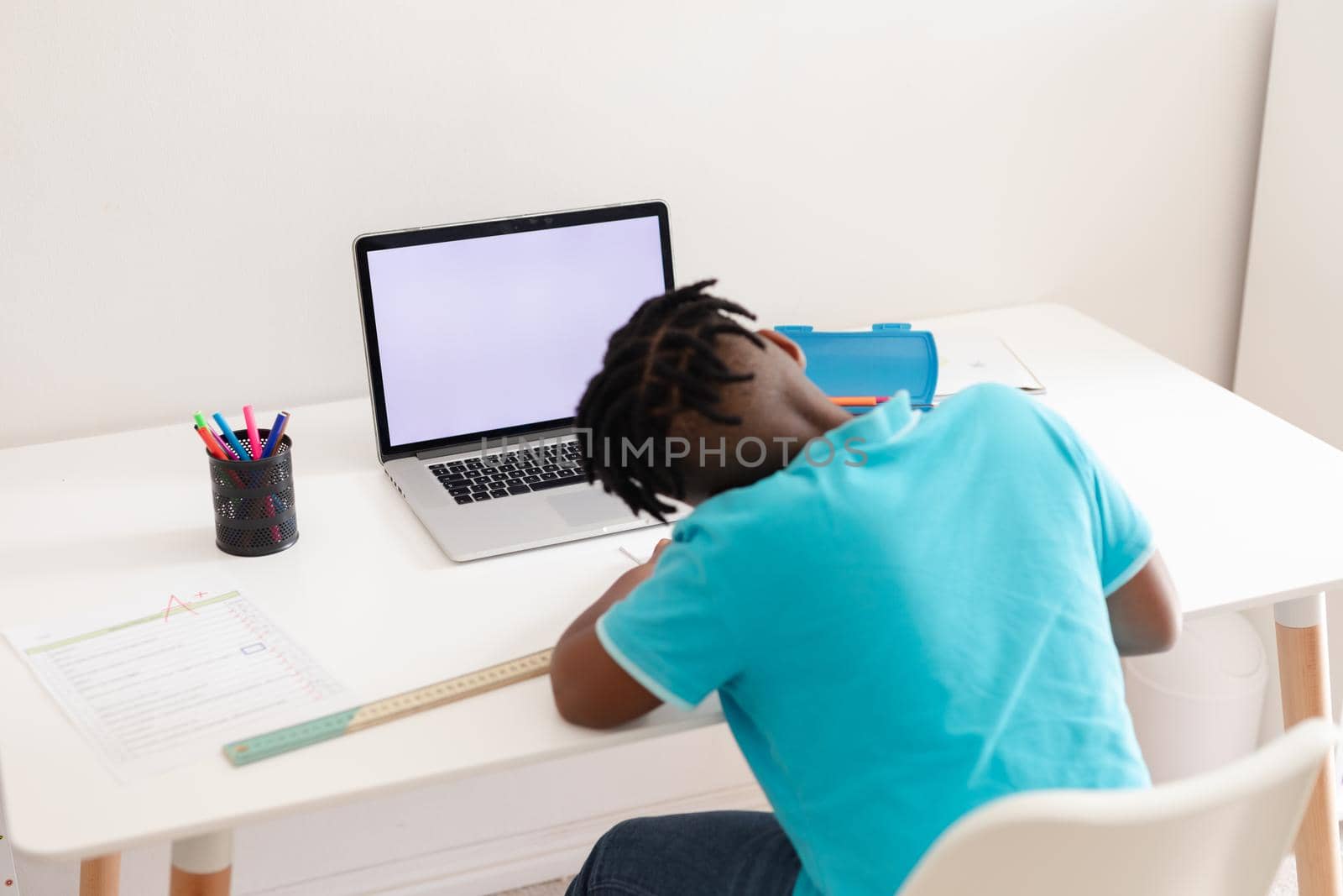Rear view of african american boy with sitting at desk with laptop doing school work. staying at home in isolation during quarantine lockdown.