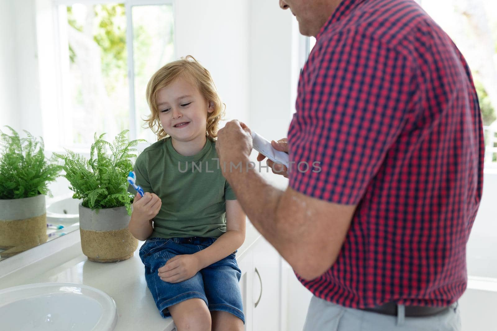 Caucasian grandfather in bathroom brushing teeth with smiling grandson sitting beside basin by Wavebreakmedia