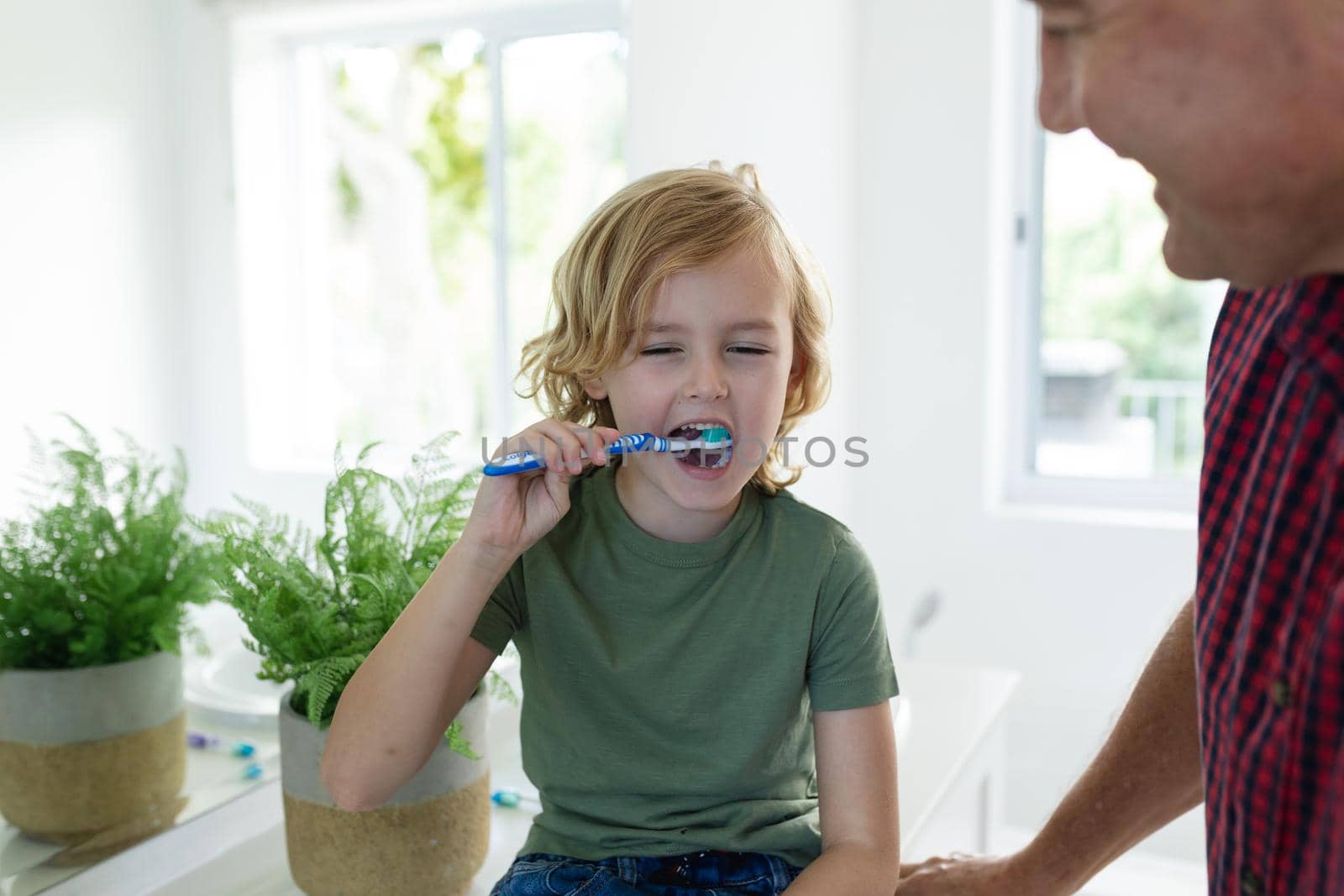 Caucasian grandfather in bathroom with grandson brushing teeth sitting beside basin. staying at home in isolation during quarantine lockdown.