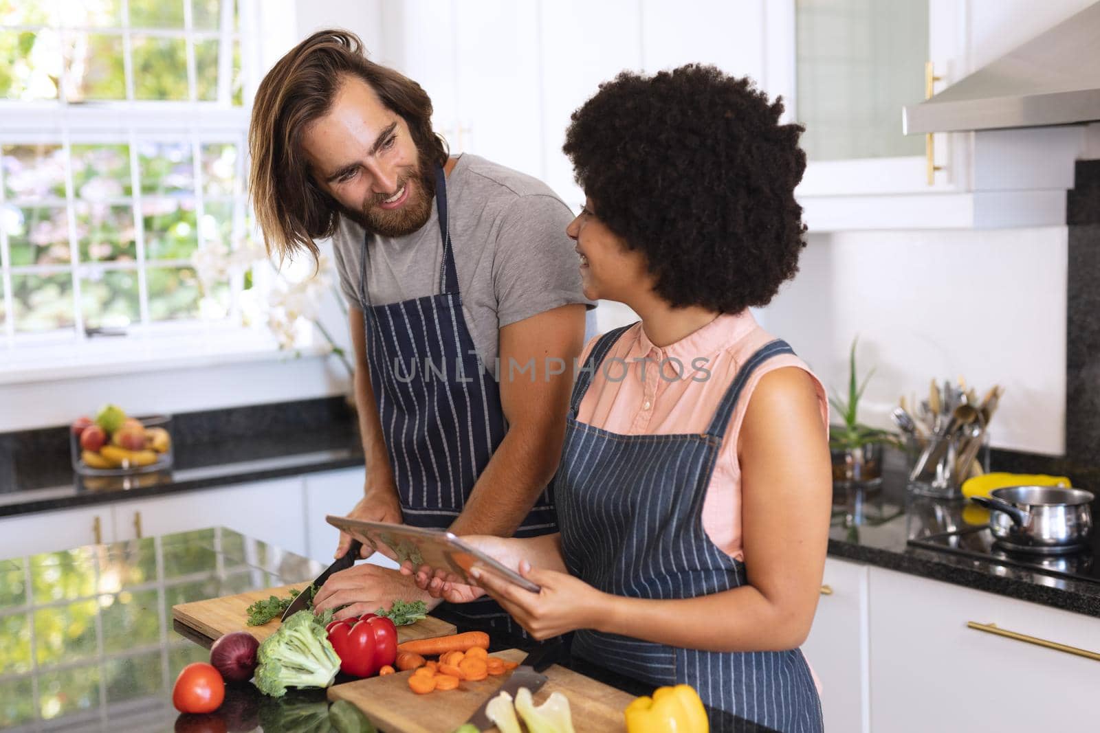 Happy diverse couple in kitchen using tablet and preparing food by Wavebreakmedia