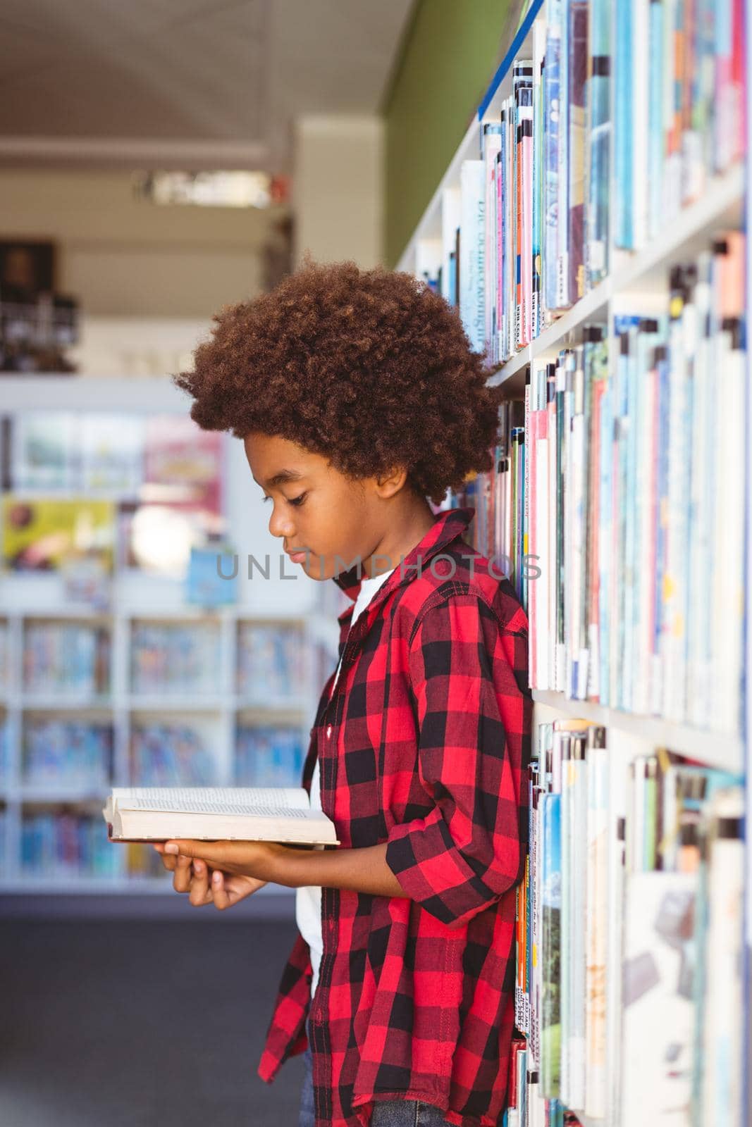 Happy african american schoolboy reading book standing in school library by Wavebreakmedia