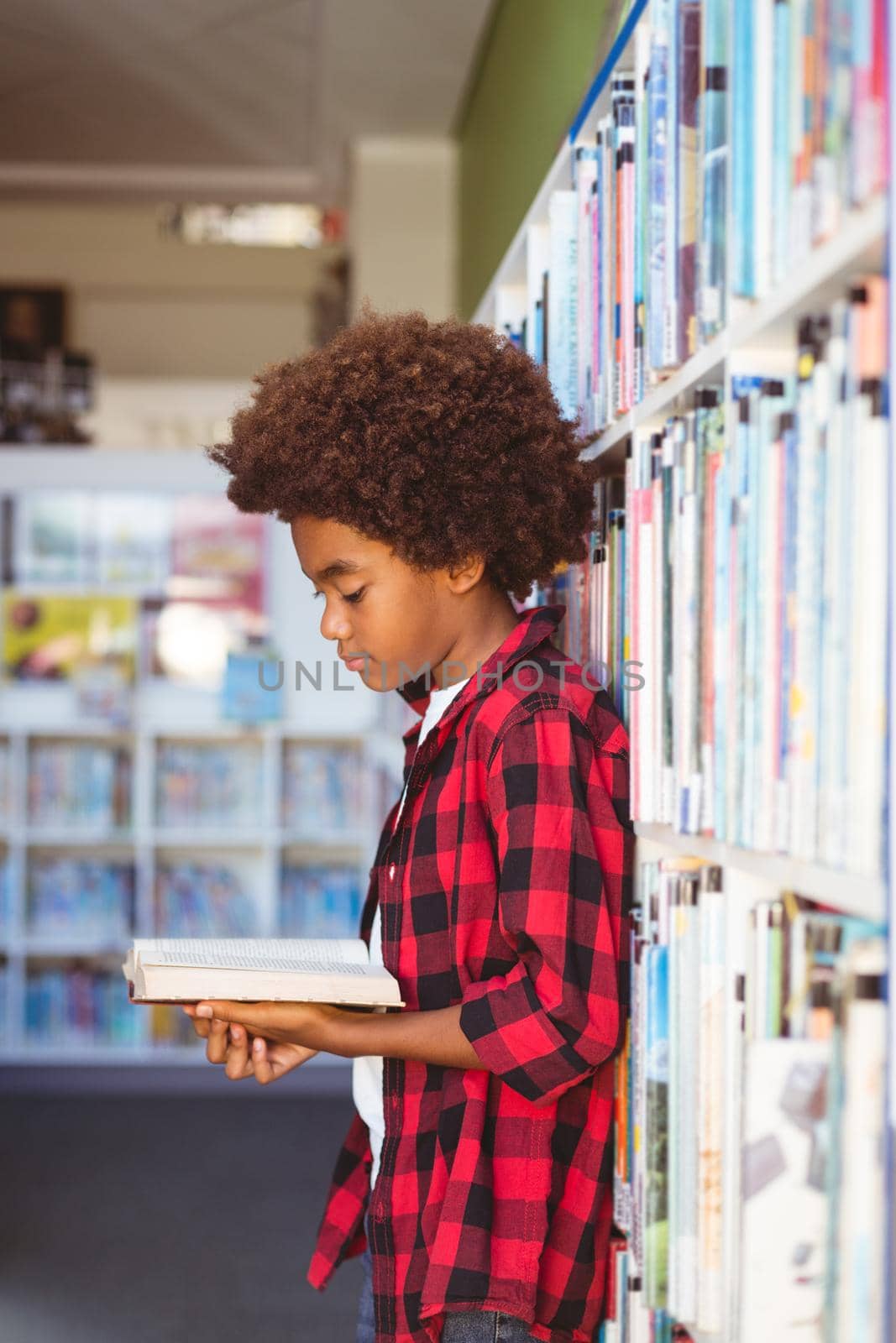 Happy african american schoolboy reading book standing in school library. childhood and education at elementary school.