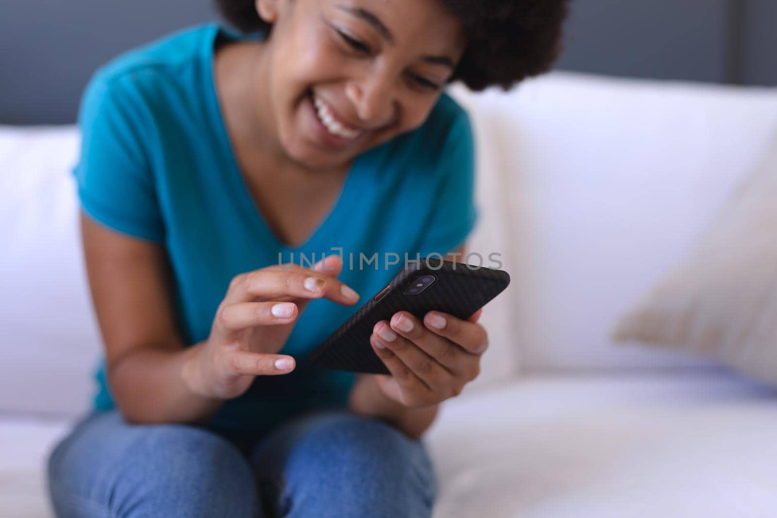 African american woman sitting on sofa using smartphone. staying at home in isolation during quarantine lockdown.