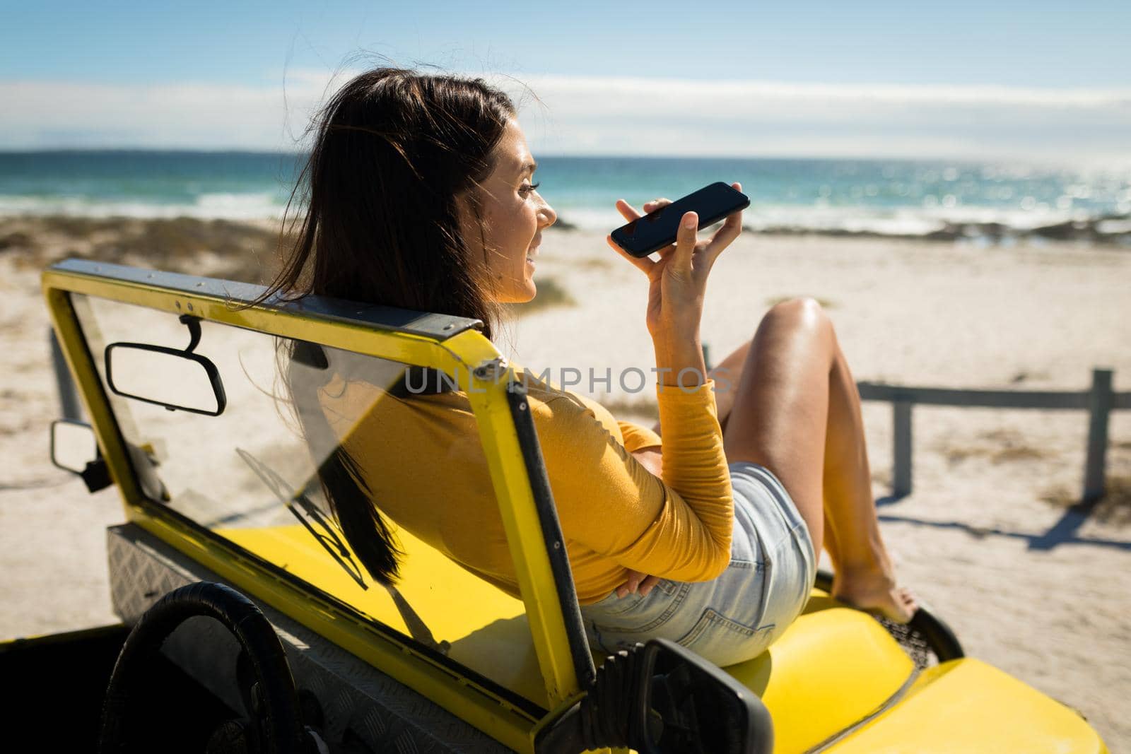 Caucasian woman lying on a beach buggy by the sea talking on smartphone. beach break on summer holiday road trip.