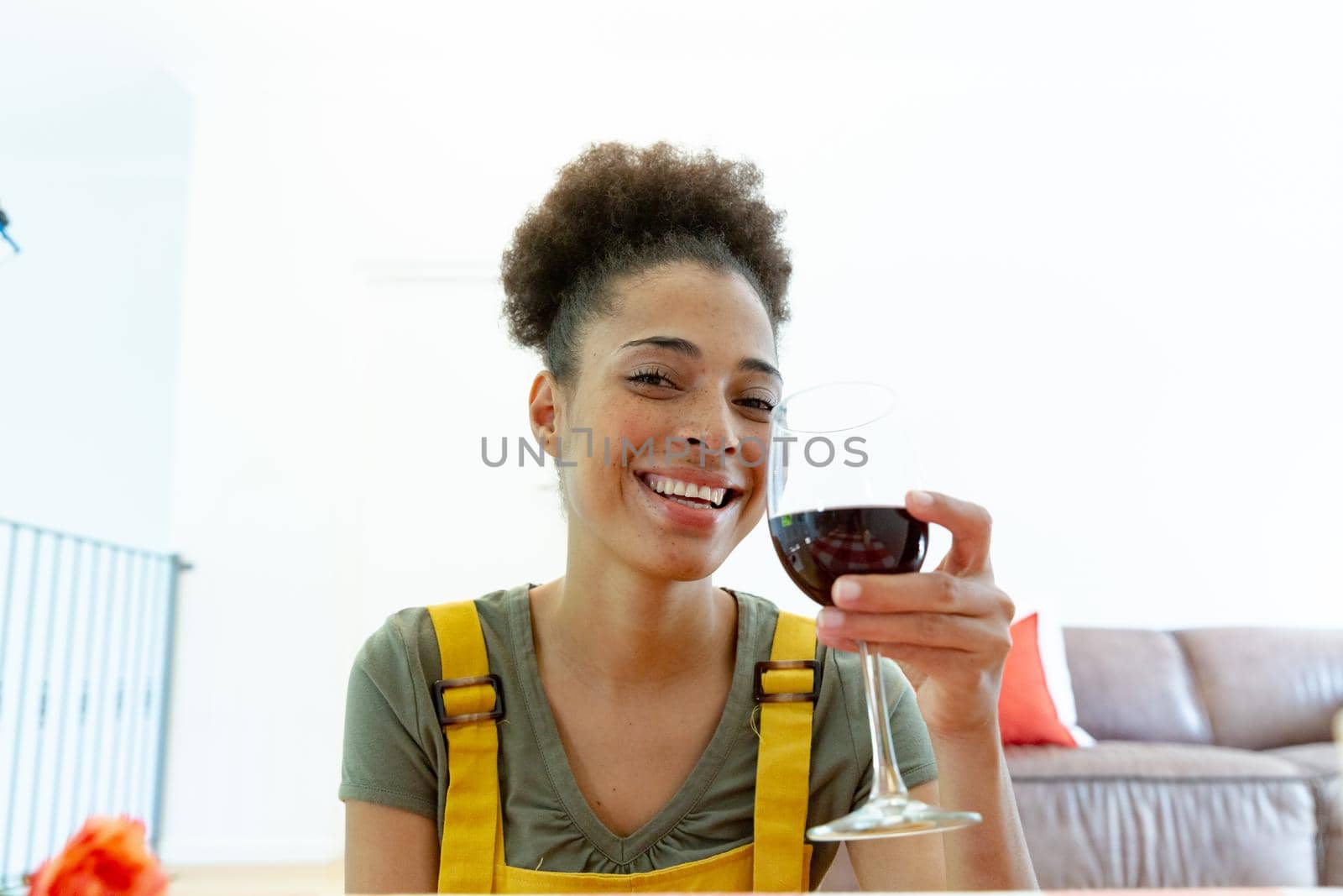Mixed race woman drinking a glass of wine and smiling at home. staying at home in isolation during quarantine lockdown.