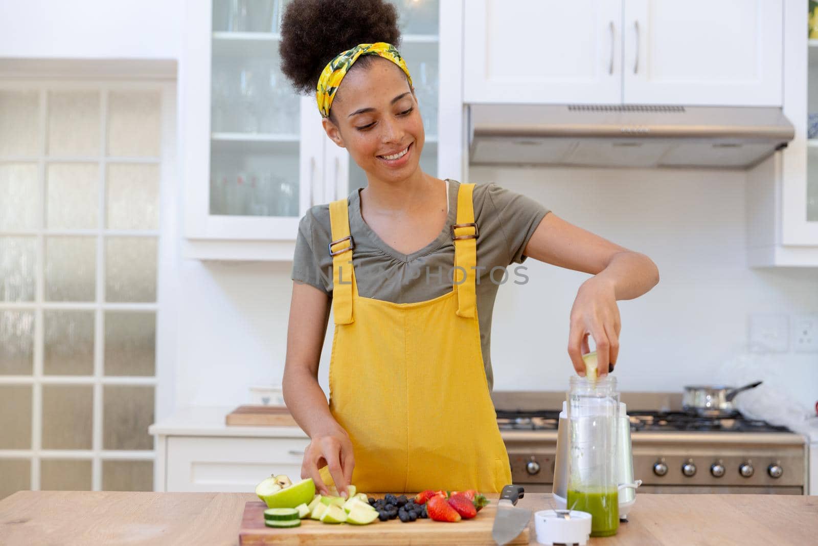 Mixed race woman making a healthy drink and smiling in a kitchen. staying at home in isolation during quarantine lockdown.