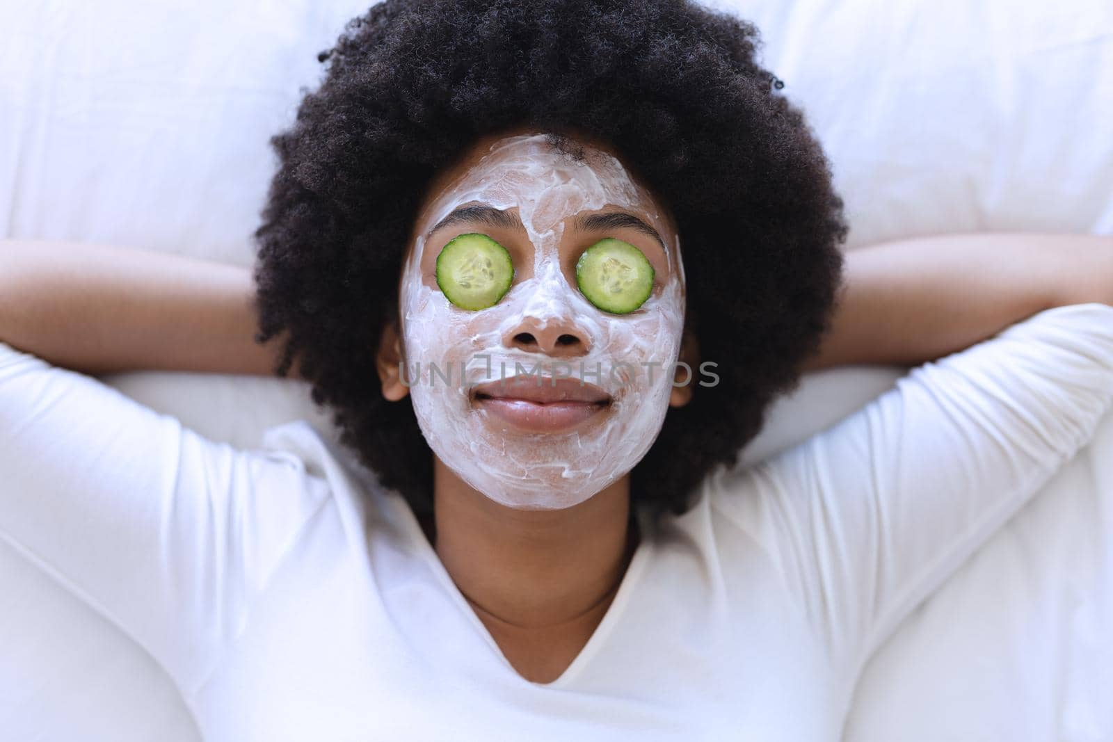 African american woman lying in bed wearing beauty mask. staying at home in isolation during quarantine lockdown.