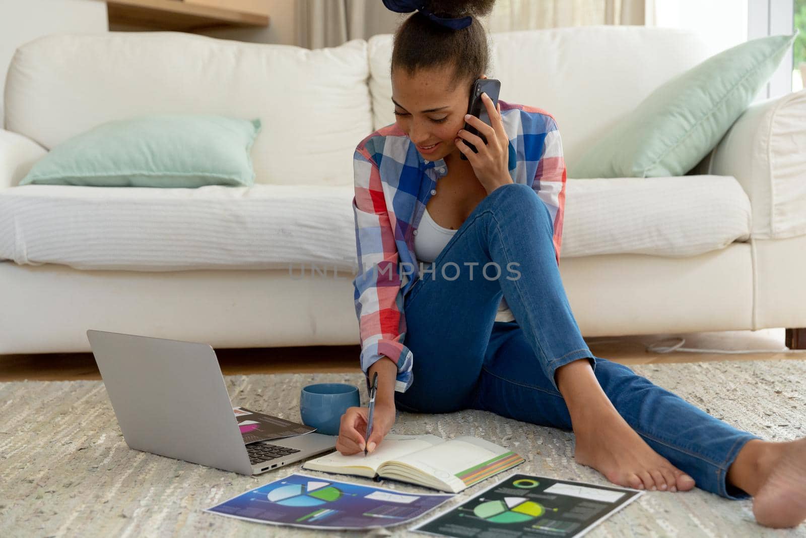 Mixed race woman sitting on the floor working from home using laptop and smartphone. staying at home in isolation during quarantine lockdown.