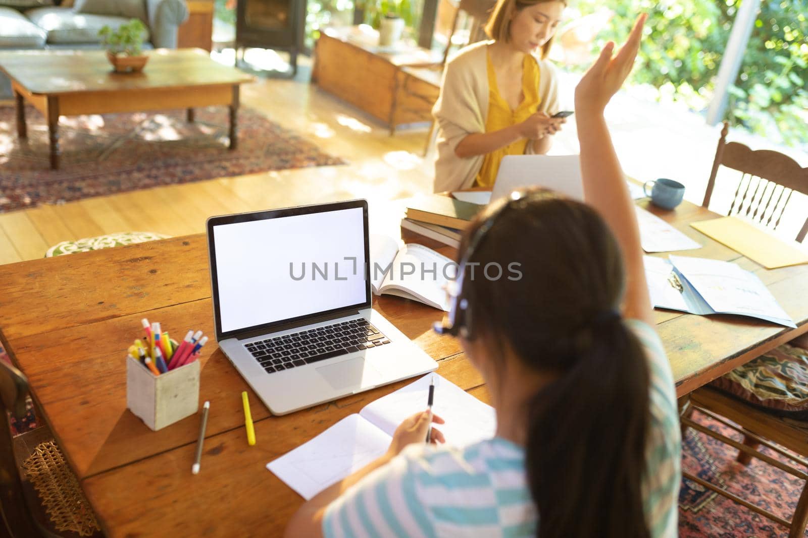 Asian girl using laptop with blank screen, raising hand, learning online her mum in background. at home in isolation during quarantine lockdown.