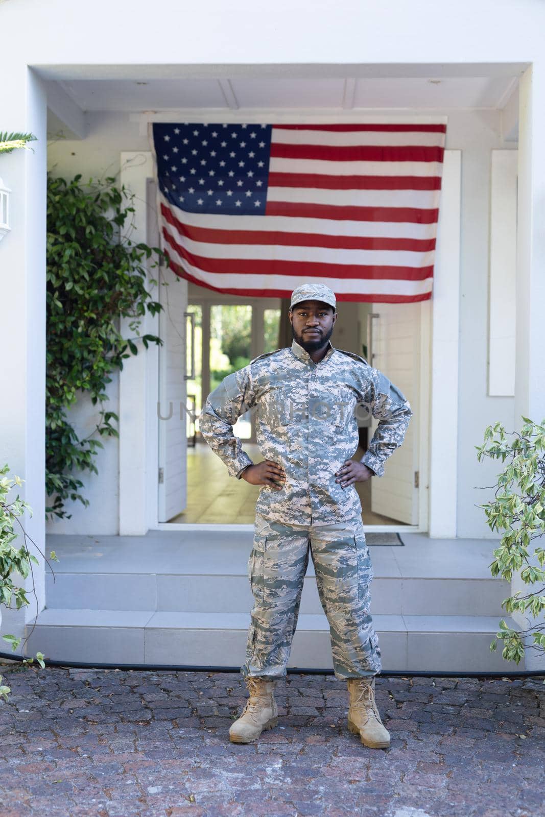 African american male soldier standing in front of american flag outside home. soldier returning home to family.