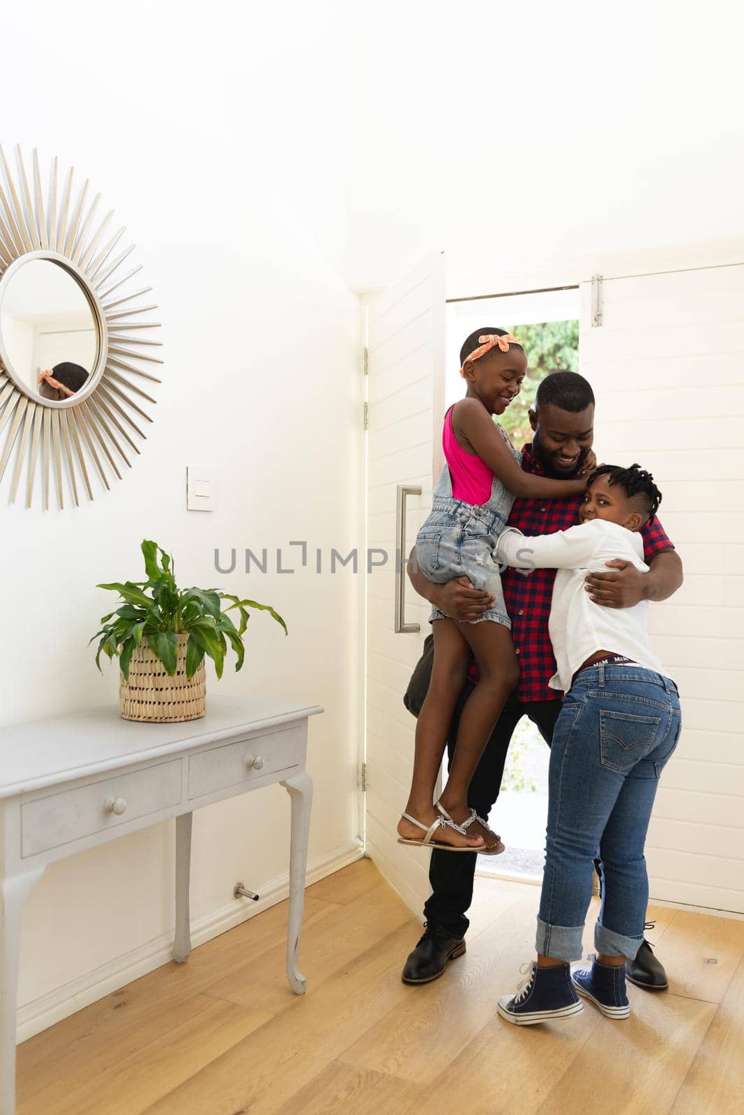 Smiling african american father returning home embracing son and daughter in hallway by Wavebreakmedia