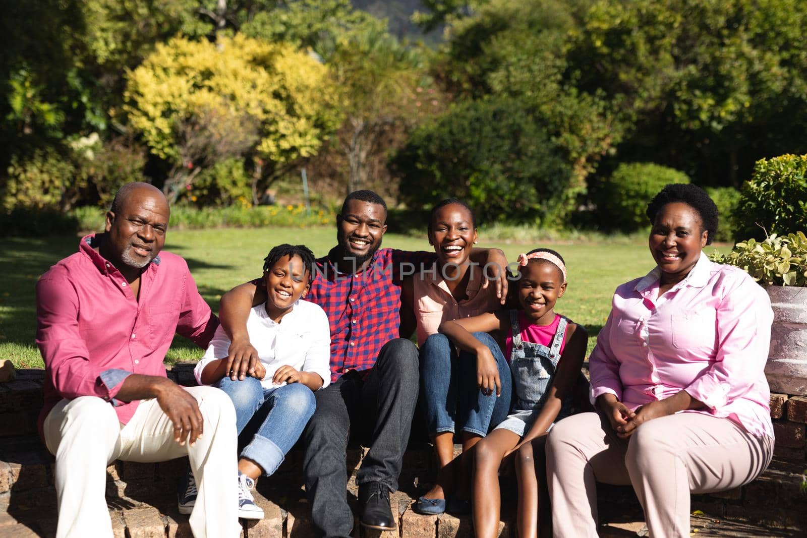 Smiling african american parents with children and their grandparents sitting embracing outdoors by Wavebreakmedia