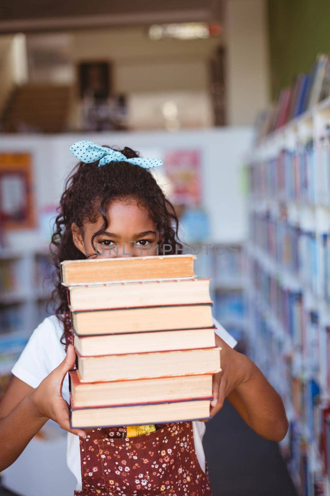 Portrait of happy african american schoolgirl carrying stack of books in school library by Wavebreakmedia