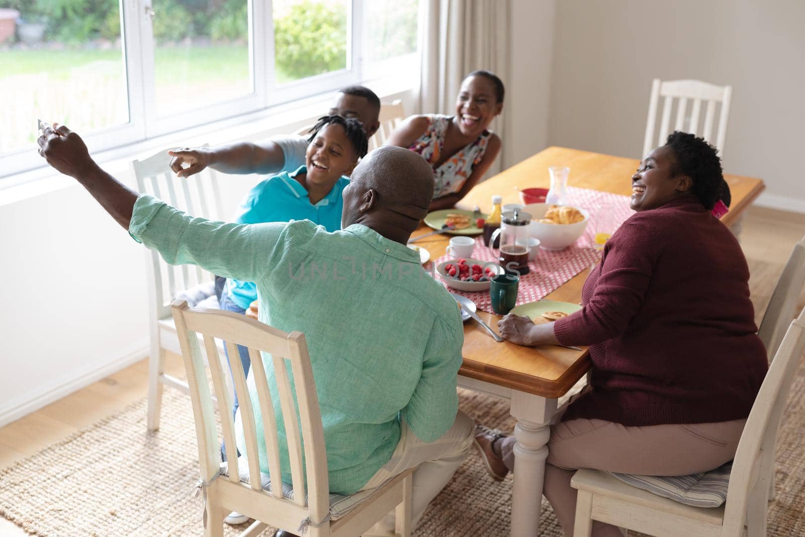 African american grandfather taking selfie with grandchildren and their parents at family meal. three generation family spending quality time together.