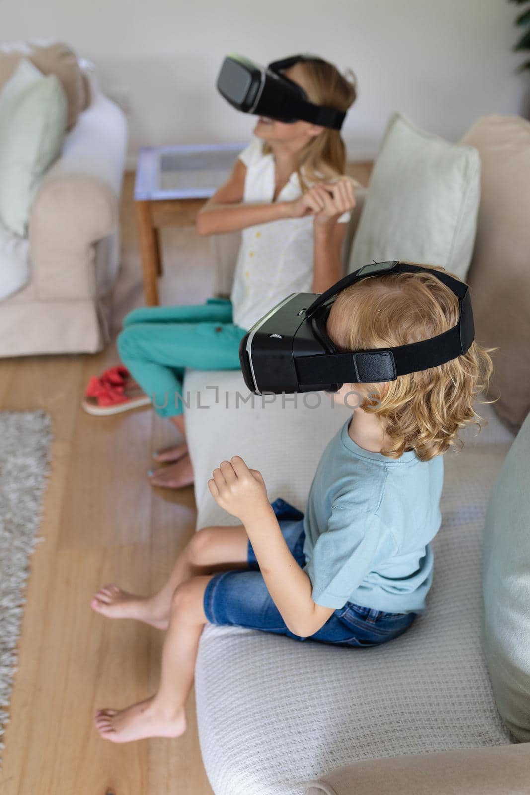 Caucasian brother and sister wearing vr headsets sitting on couch facing each other. staying at home in isolation during quarantine lockdown.