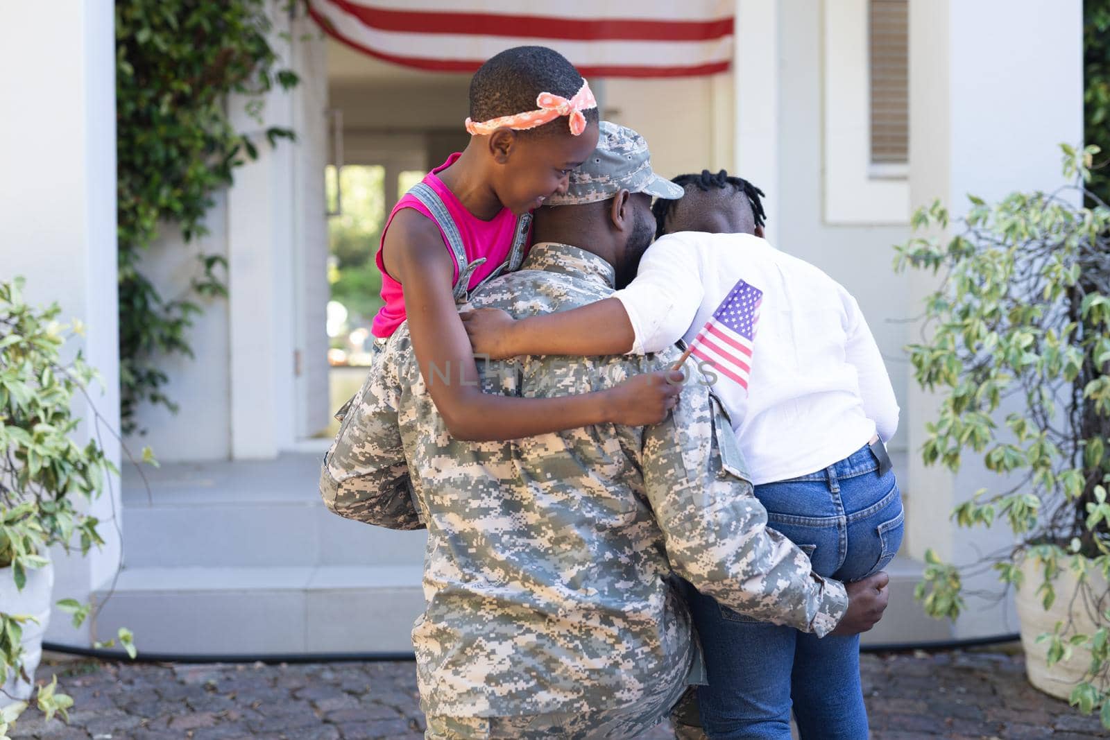 Rear view of african american soldier father hugging son and daughter in front of house. soldier returning home to family.