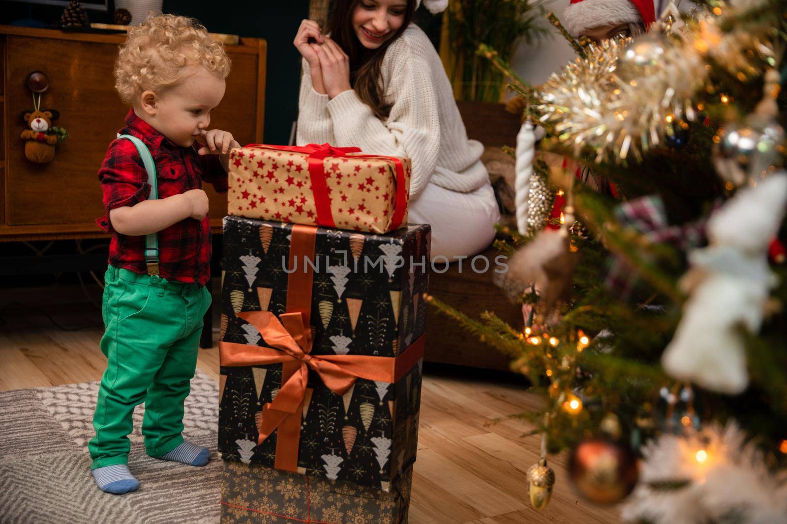 A two-year-old child looks at wrapped gift boxes standing next to a Christmas tree. Traditional Christmas in Poland.