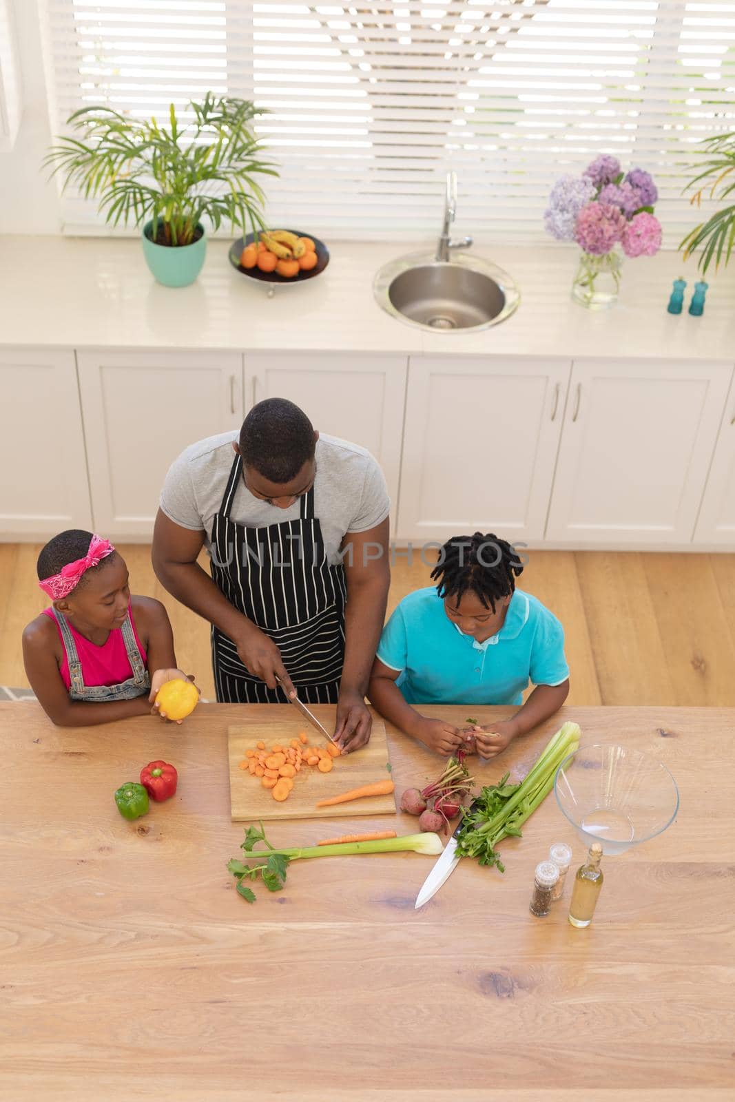 High angle view of african american father teaching daughter and son cooking in the kitchen. staying at home in isolation during quarantine lockdown.