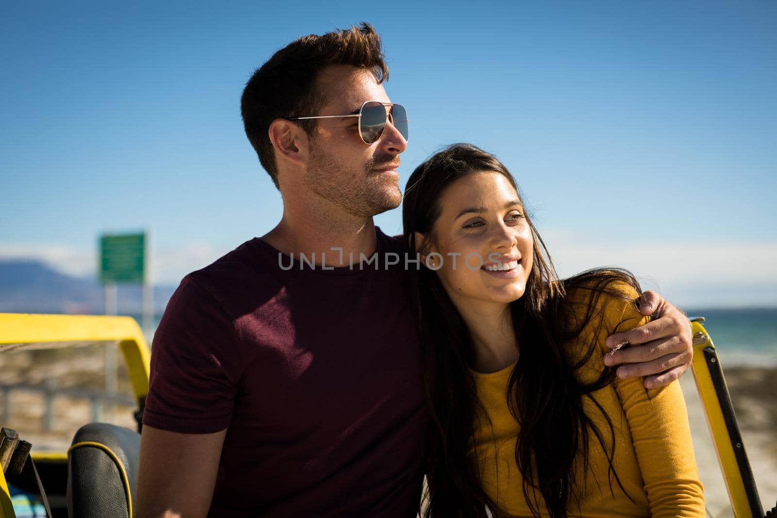 Happy caucasian couple sitting on beach buggy by the sea embracing. beach break on summer holiday road trip.