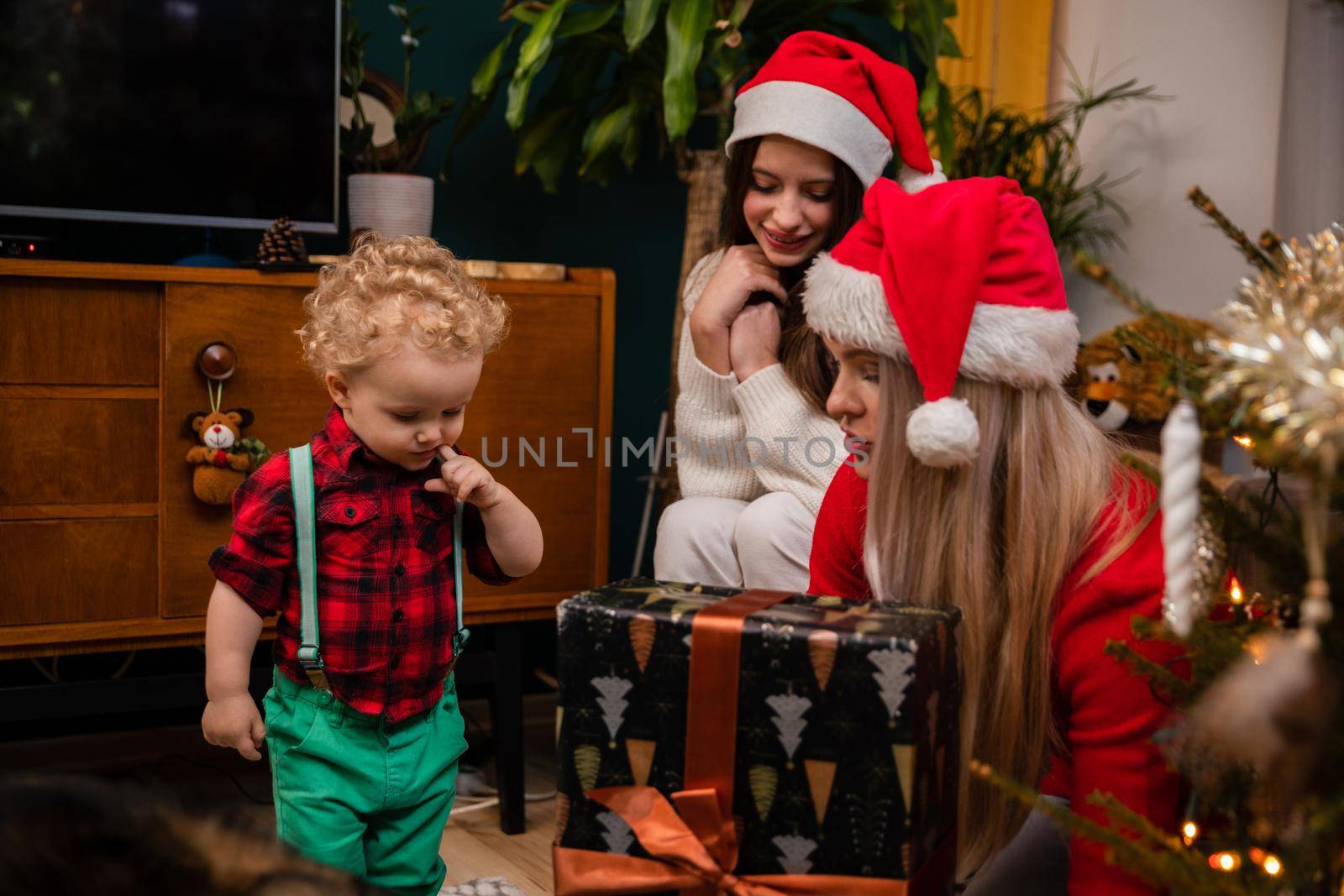 A woman sits next to presents and talks to her son about traditions and Christmas. A little two-year-old boy with curly blond hair.