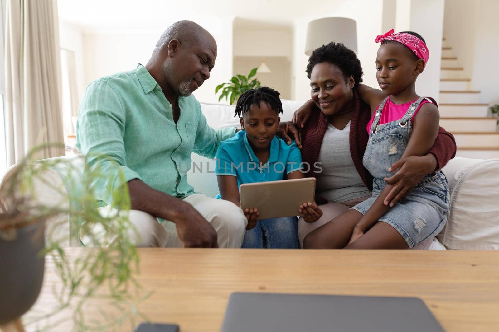 Happy african american grandfather and grandmother on couch with grandchildren looking at tablet. happy family spending time together at home.