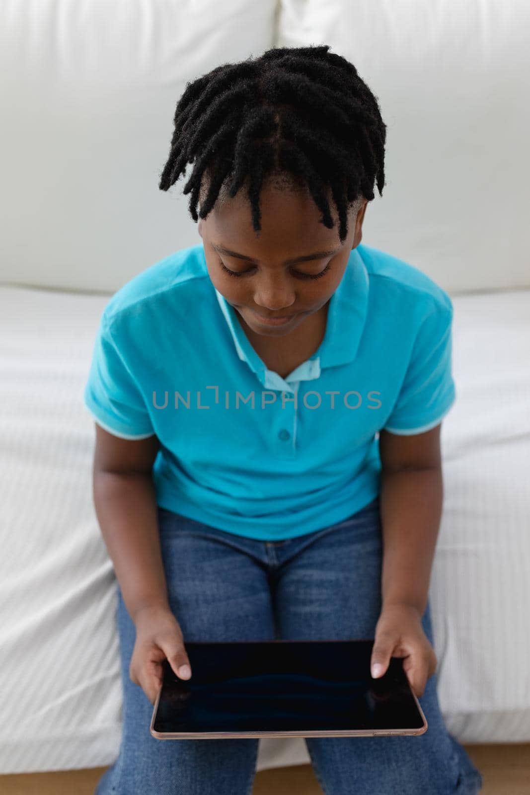 High angle view of african american boy with short dreadlocks sitting on couch using digital tablet by Wavebreakmedia