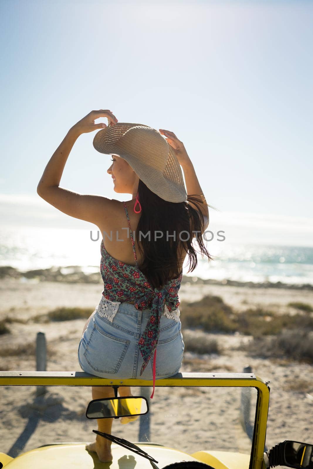Happy caucasian woman sitting on beach buggy by the sea wearing straw hat looking toward sea by Wavebreakmedia