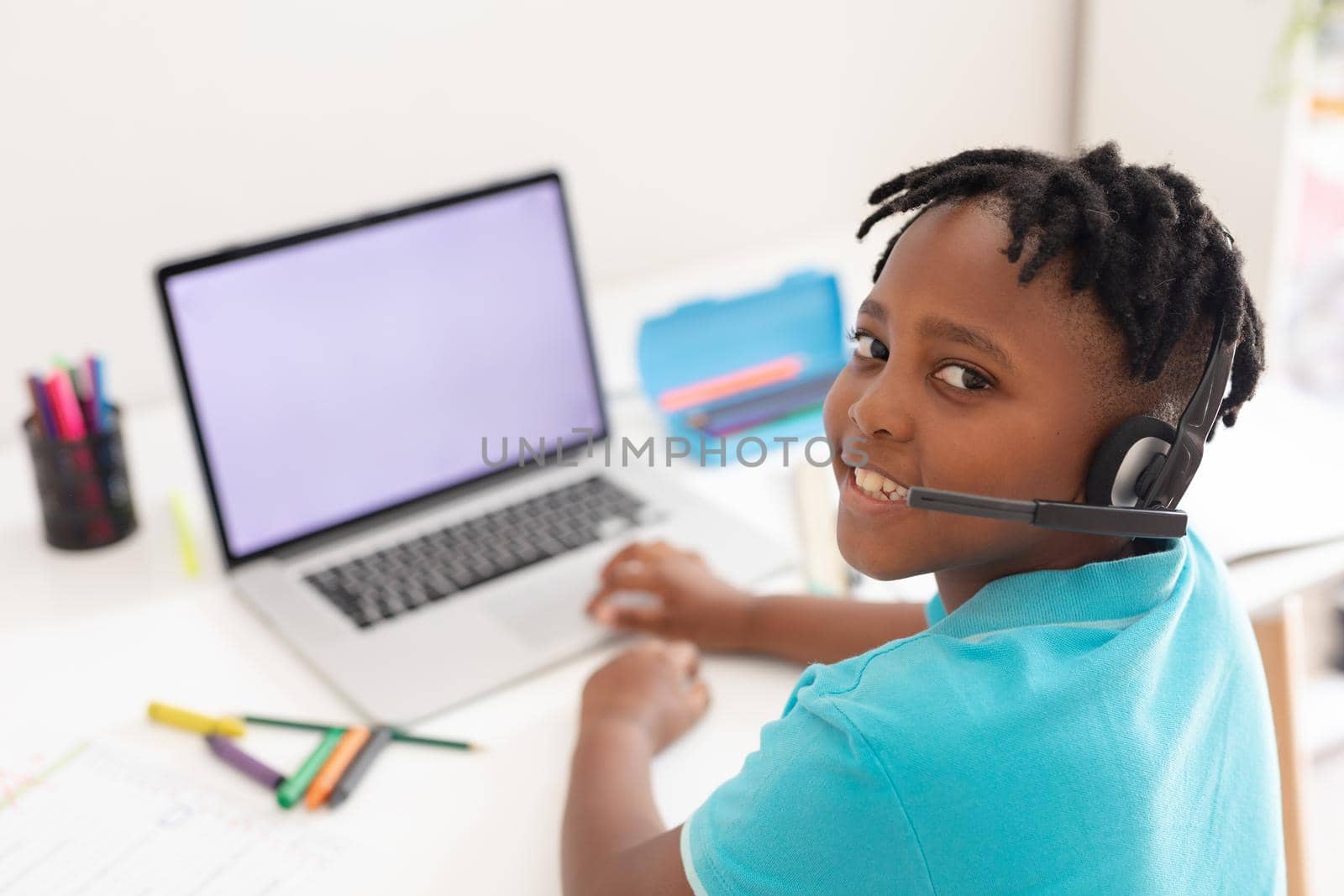 Portrait of african american boy wearing headset at desk using laptop for online school lesson. staying at home in isolation during quarantine lockdown.