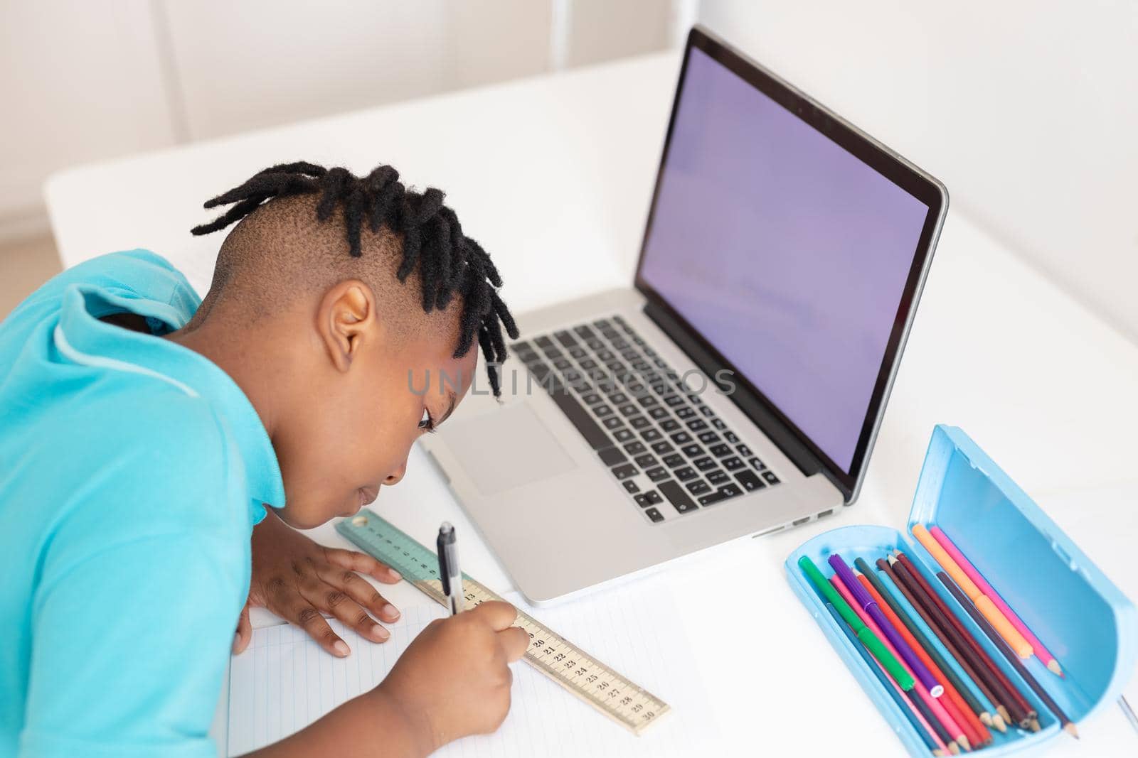 African american boy at desk using laptop with copy space for online school lesson. staying at home in isolation during quarantine lockdown.