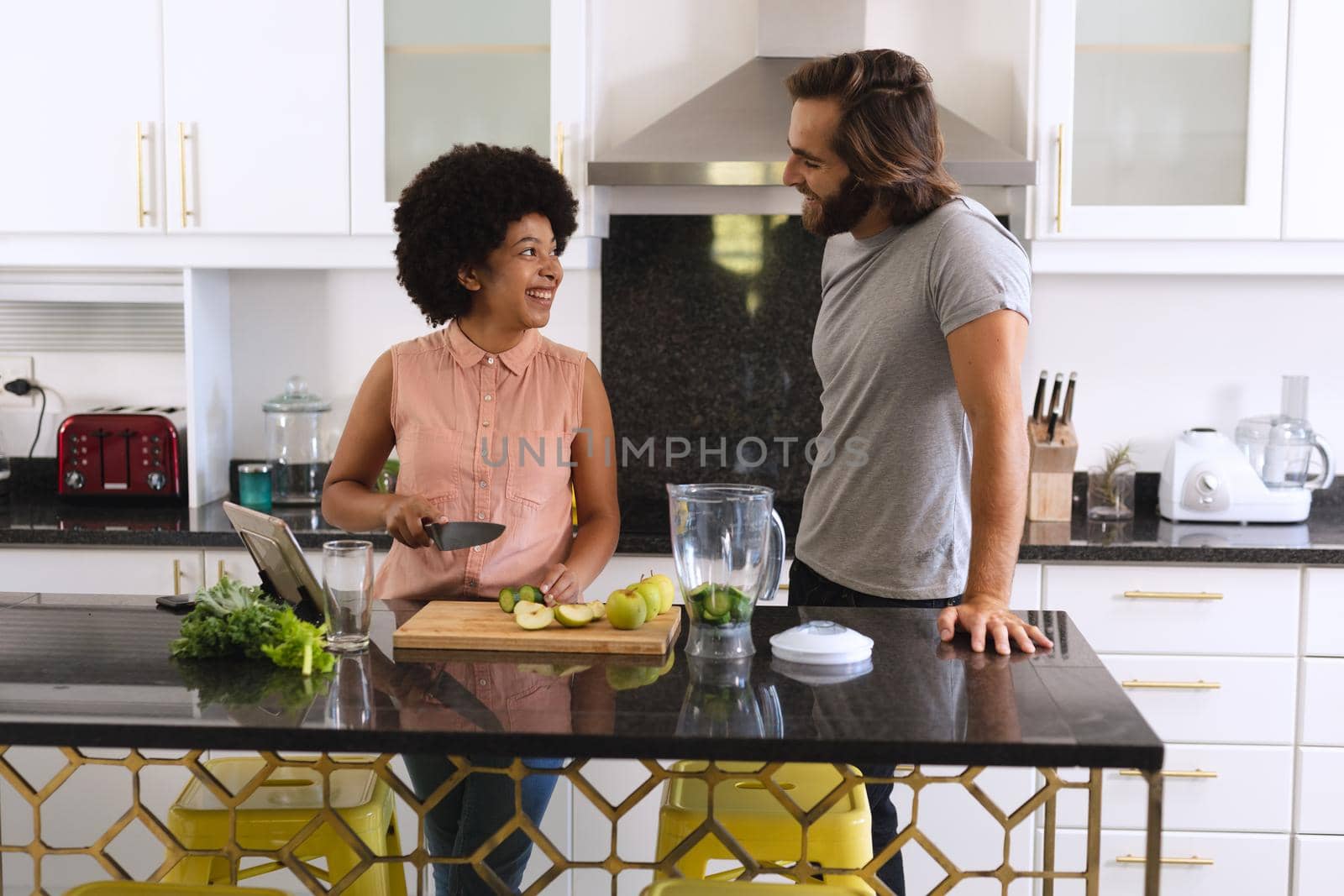 Happy diverse couple in kitchen smiling and making health drink by Wavebreakmedia