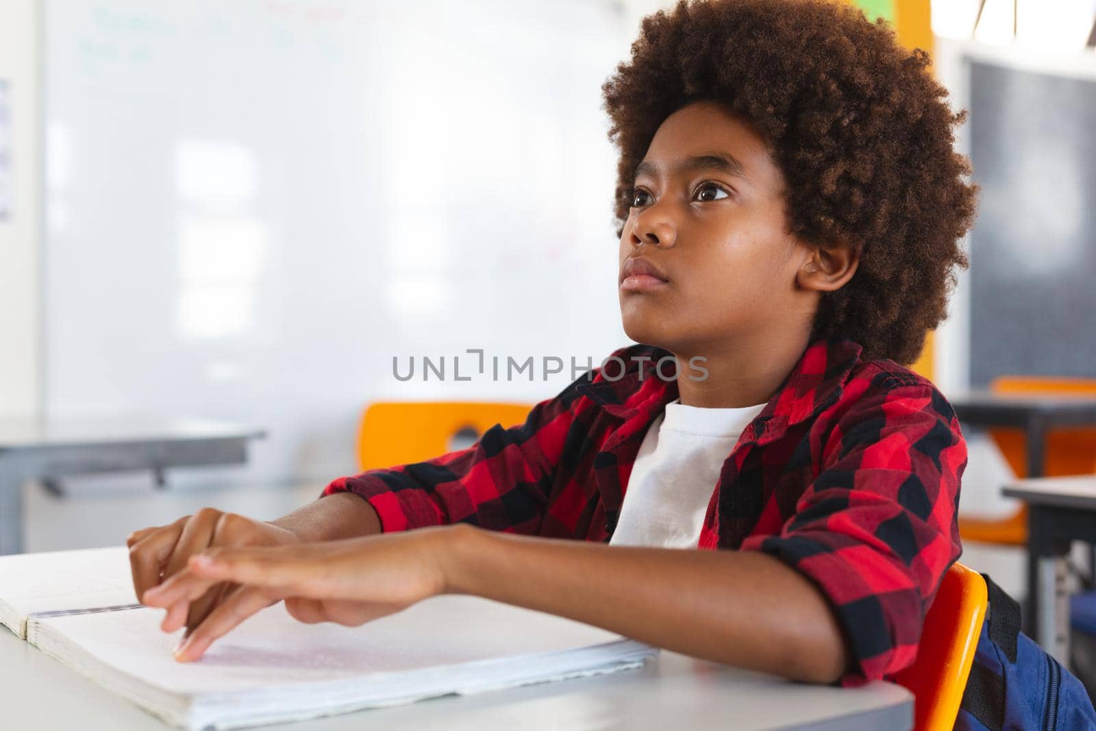 Blind african american schoolboy sitting at desk in classroom reading braille book with fingers by Wavebreakmedia