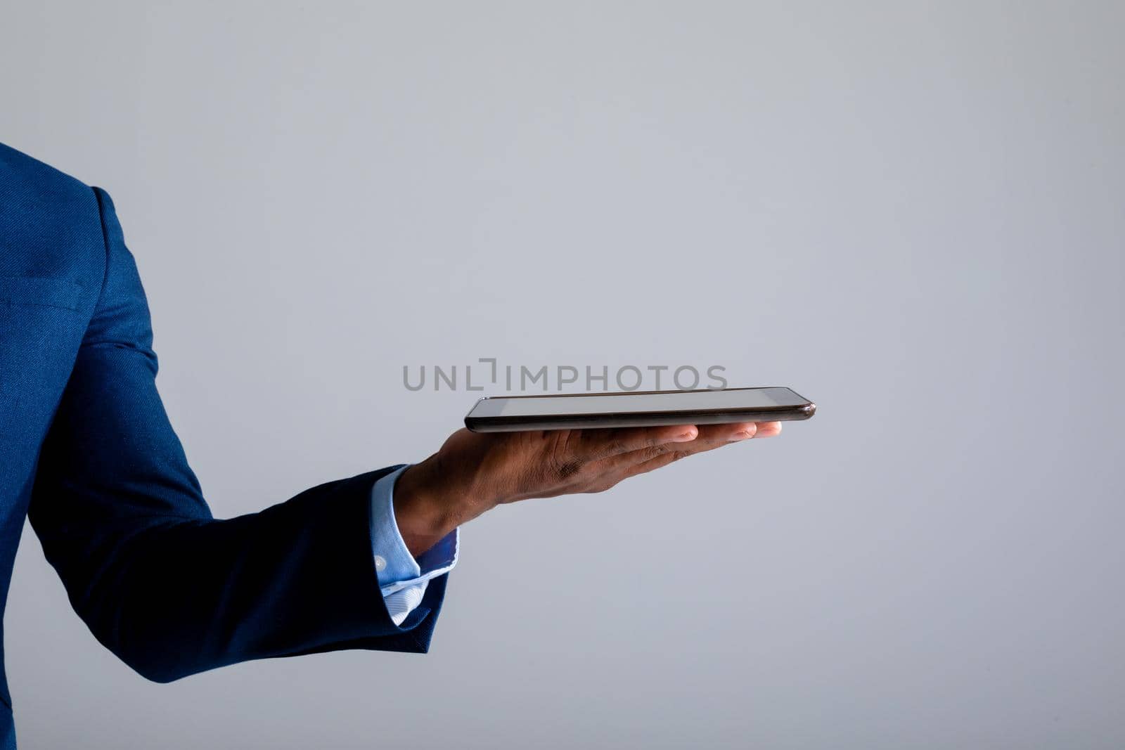 Mid section of african american businessman holding digital tablet against grey background. business, professionalism and technology concept