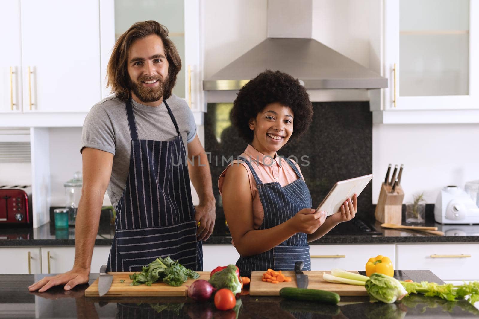 Portrait of happy diverse couple in kitchen smiling and using tablet by Wavebreakmedia