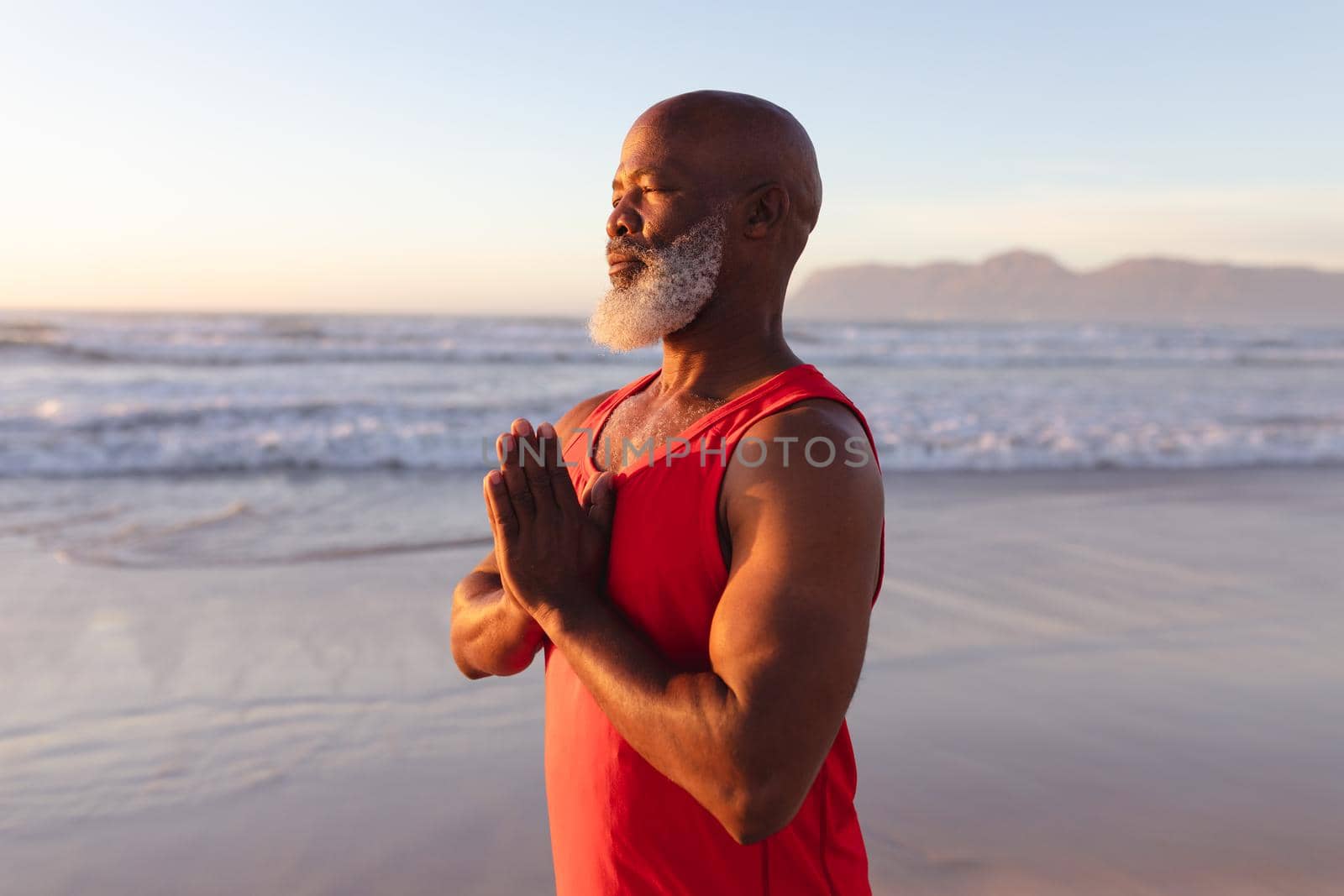 Senior african american man with folded hands meditating and practicing yoga at the beach by Wavebreakmedia