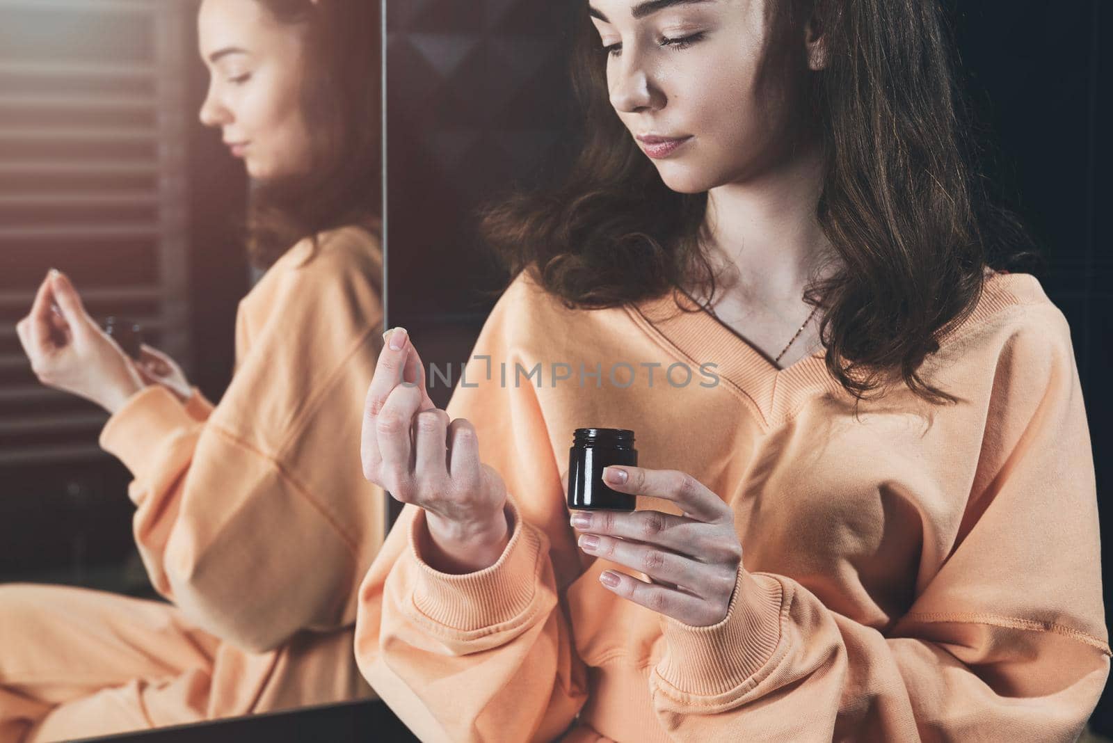 Woman is holding an open jar of cream and applies a small amount of the product to her hand. Concept of skin care, testing and selection of high-quality natural and organic cosmetics. Closeup