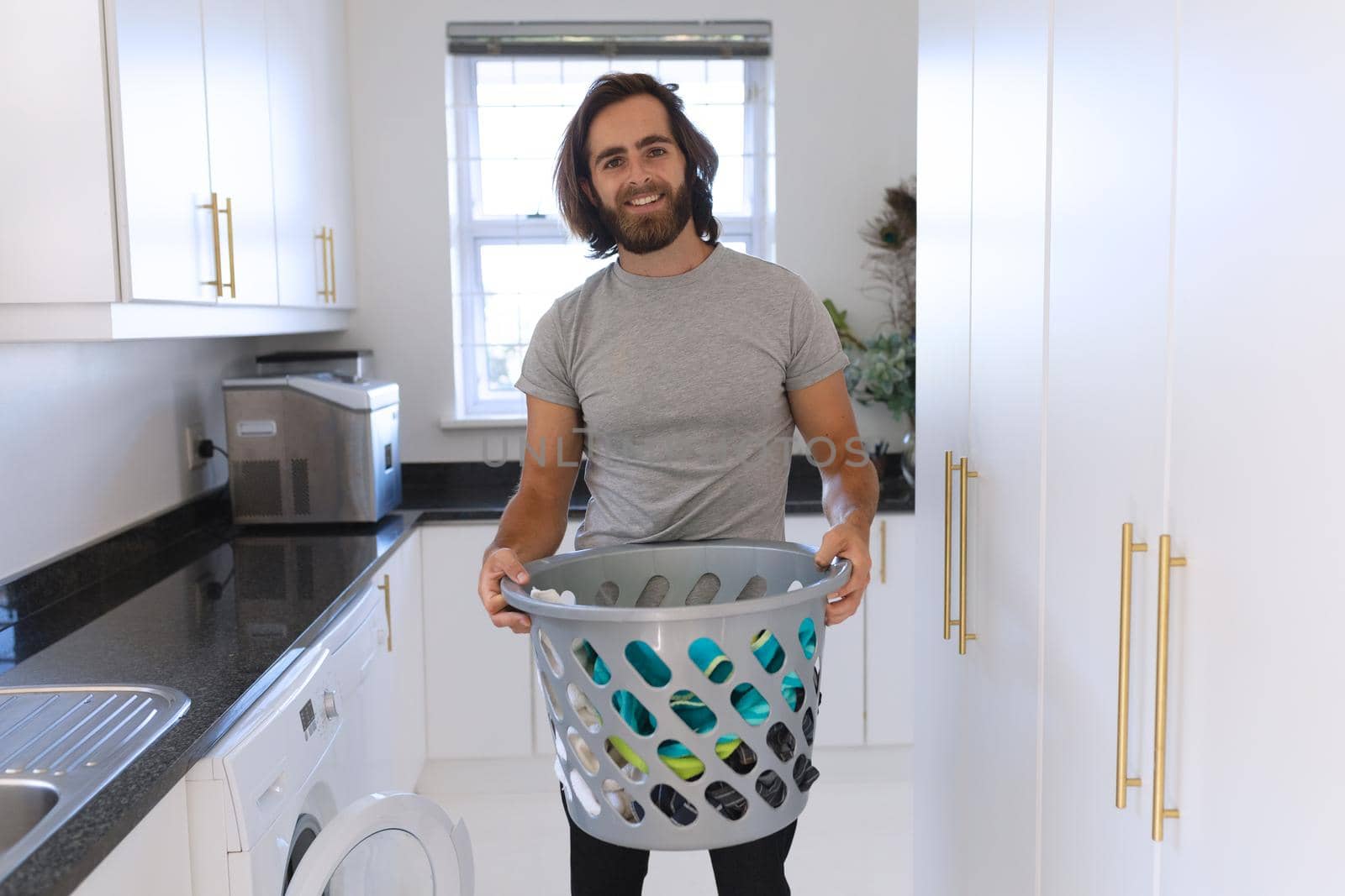 Portrait of caucasian man wearing gray tshirt and doing laundry. staying at home in isolation during quarantine lockdown.