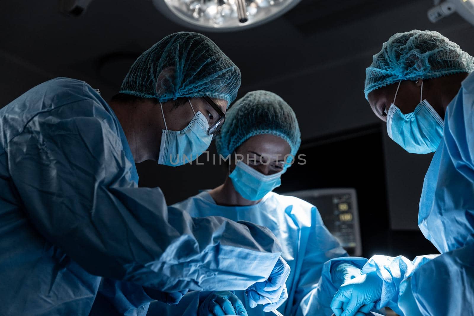Diverse group of male and female surgeons in operating theatre wearing face masks performing surgery by Wavebreakmedia
